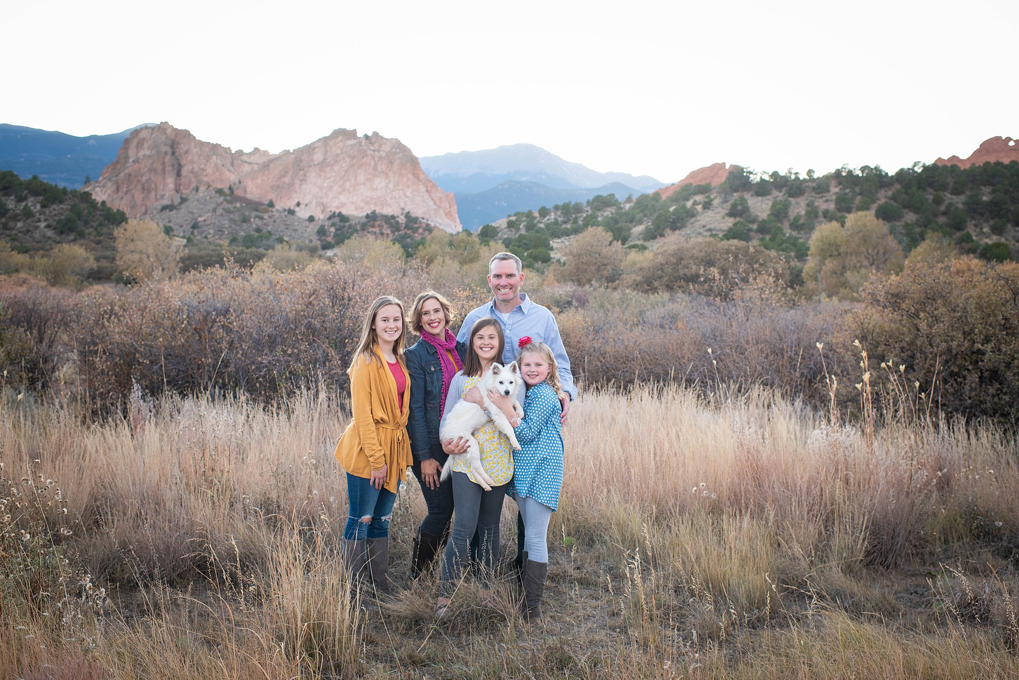 family of 5 huddling with each other in a field and smiling Colorado Springs Pediatrician