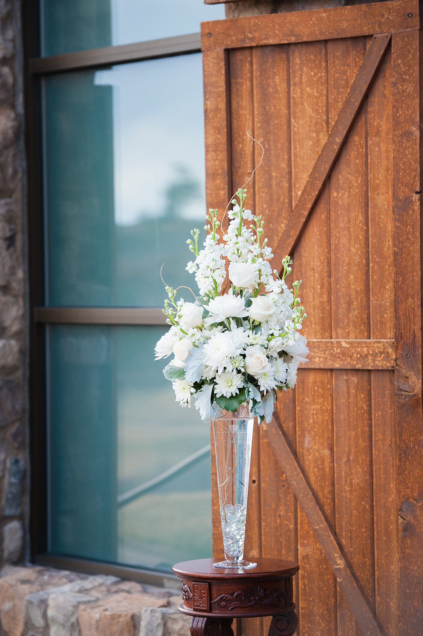 White floral arrangement sits in a glass vase on a wooden table outside