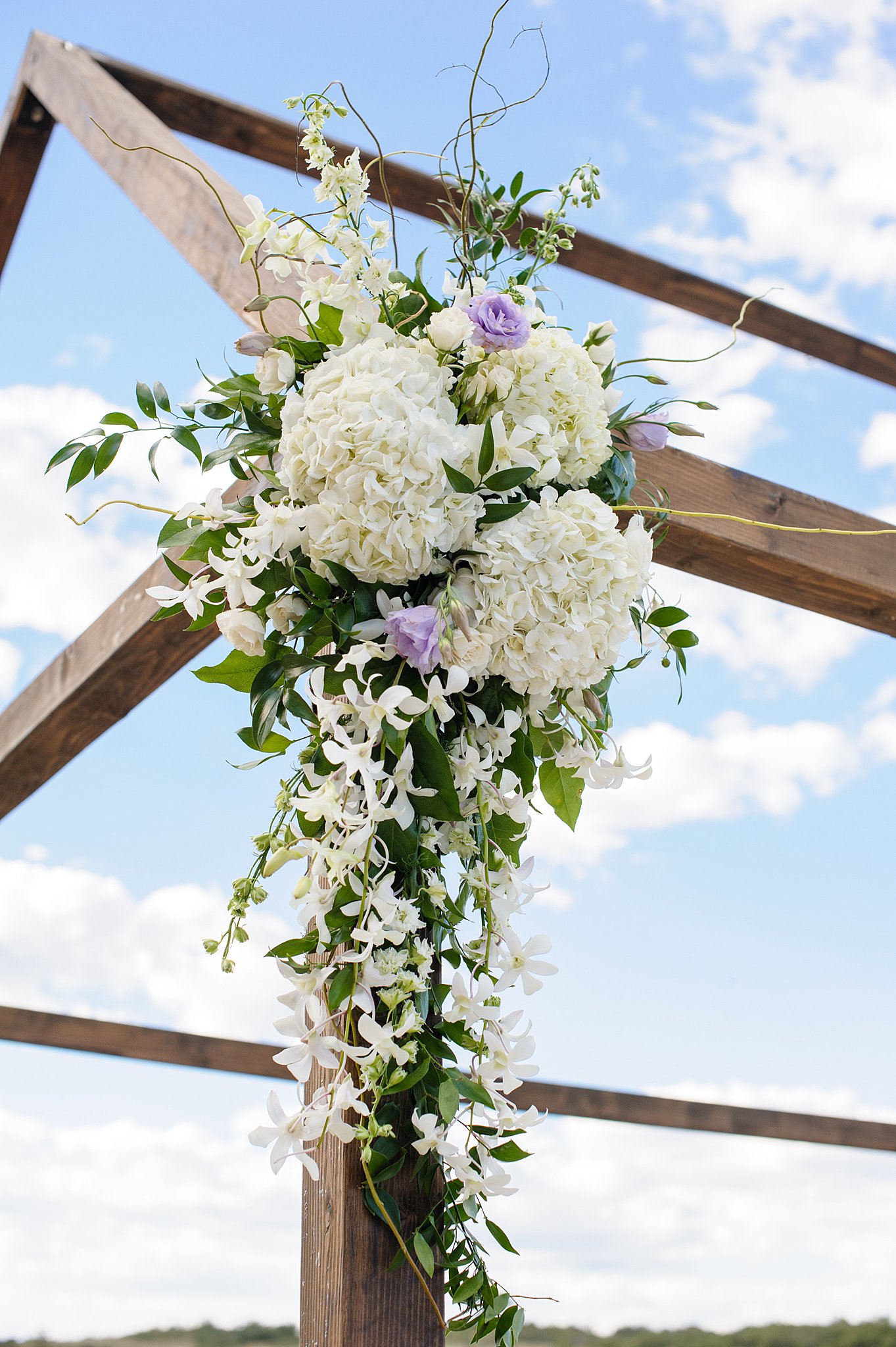 White and purple wedding flower decorations hang on a wooden arbor Colorado springs wedding florists