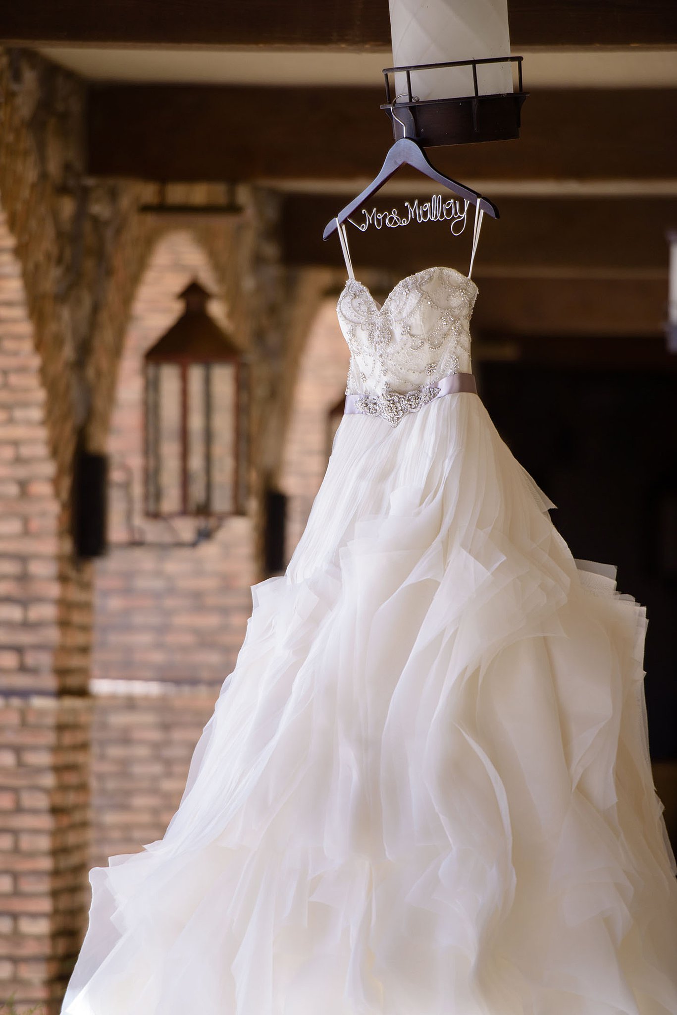 White wedding dress with silver belt hangs on a lantern in a n outdoor brick hallway