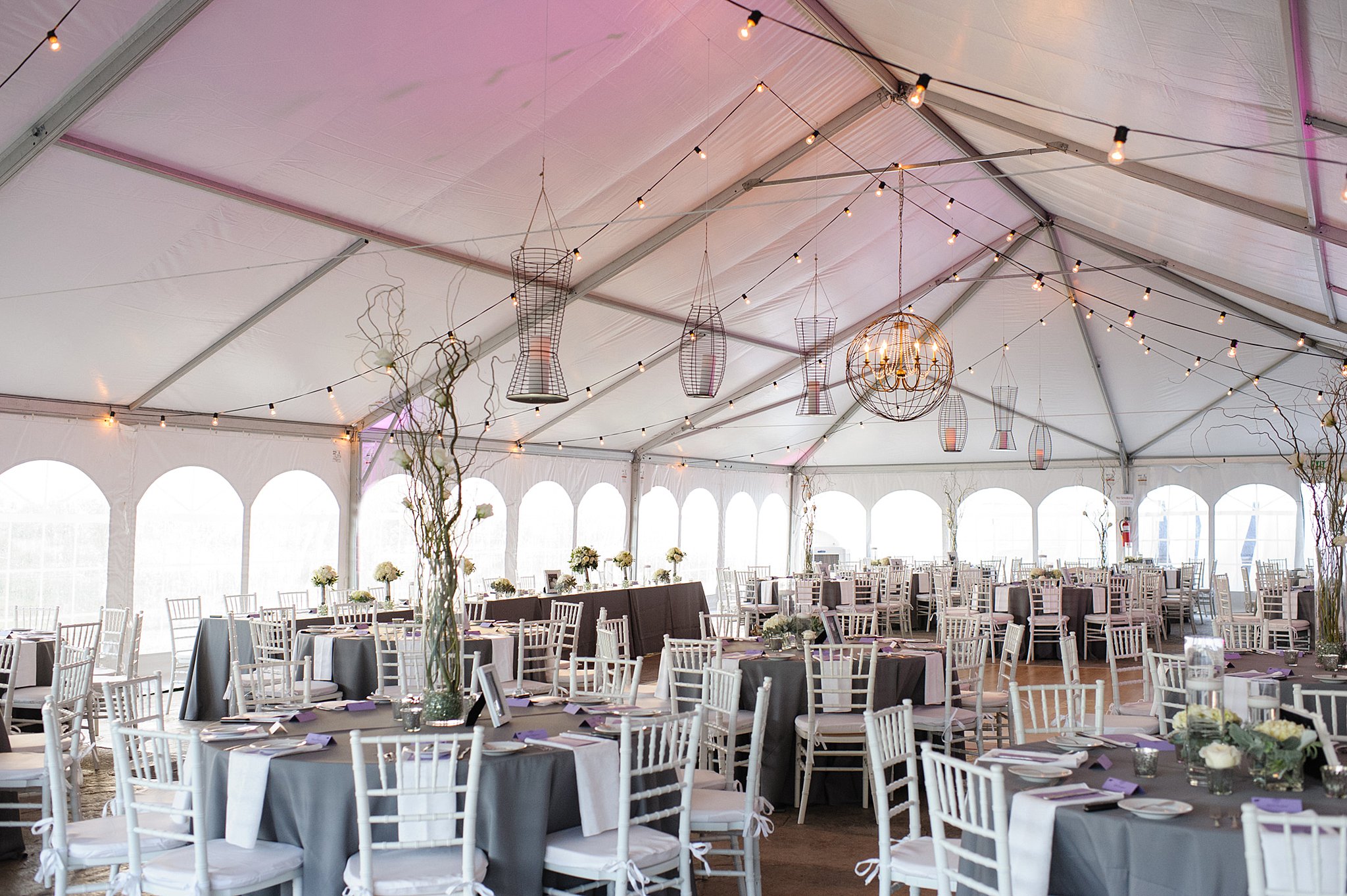 A tent wedding reception is set up with hanging lights and white chairs the club at flying horse wedding