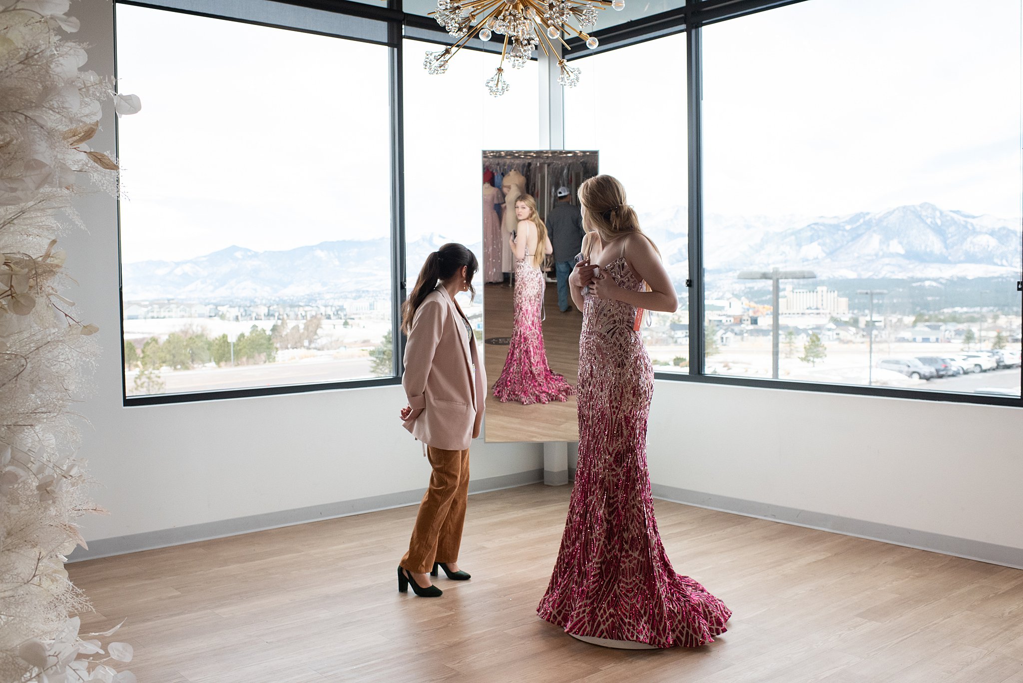 a woman trying a pink gown checks a mirror in front of many windows Something New Boutique