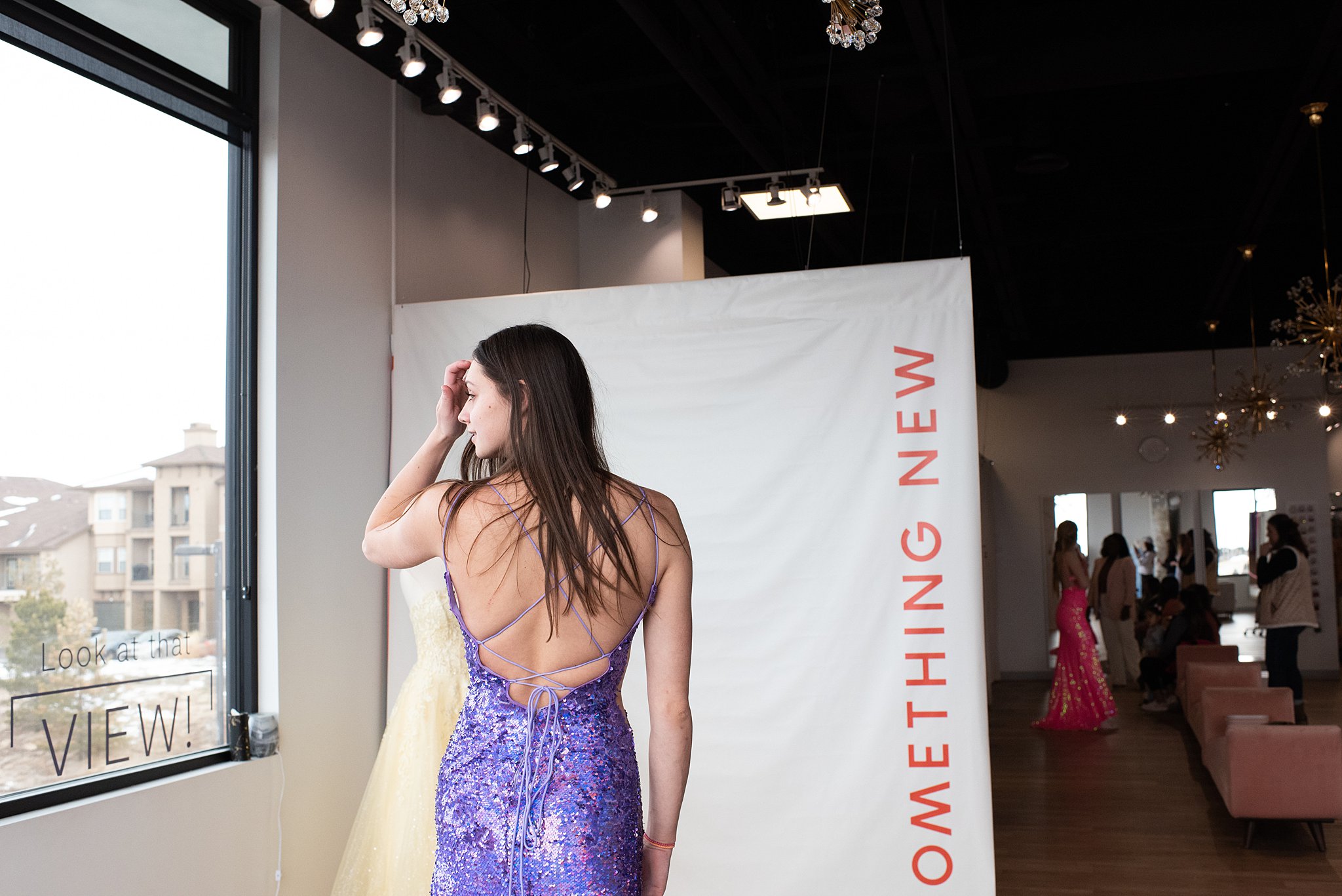 a woman in a backless purple sequin dress stands in front of a window