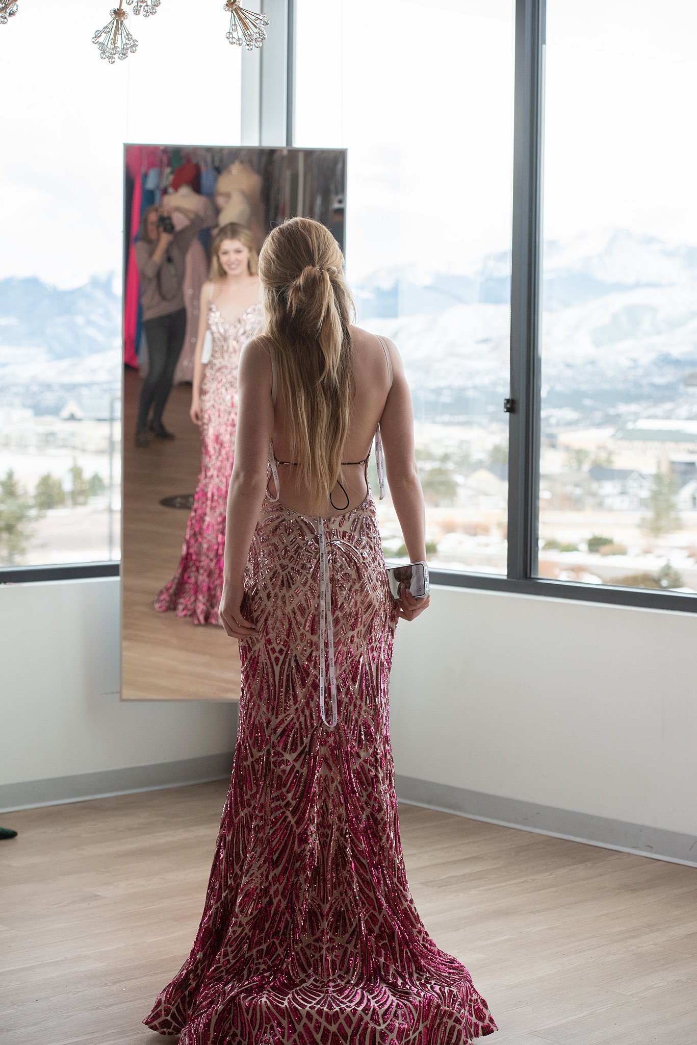 Woman in a sparkly patterned backless red dress stands in front of a mirror Something New Boutique