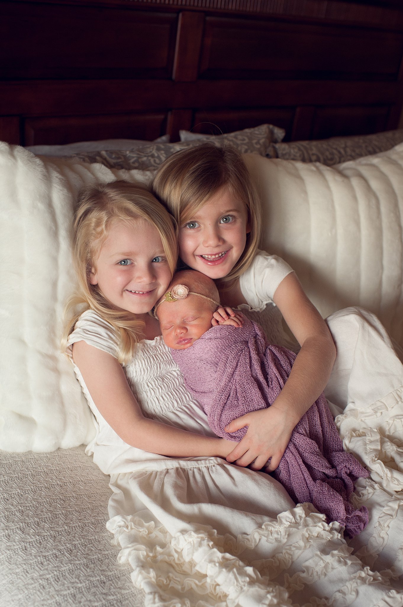 Two young sisters lay in a bed while holding their sleeping newborn sibling Wow chiropractic colorado springs