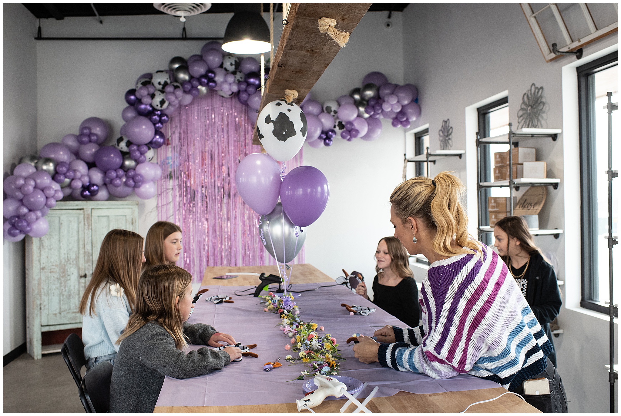 A woman leads girls in an arts and crafts event surrounded by purple, silver and cow pattern balloons colorado springs event planner