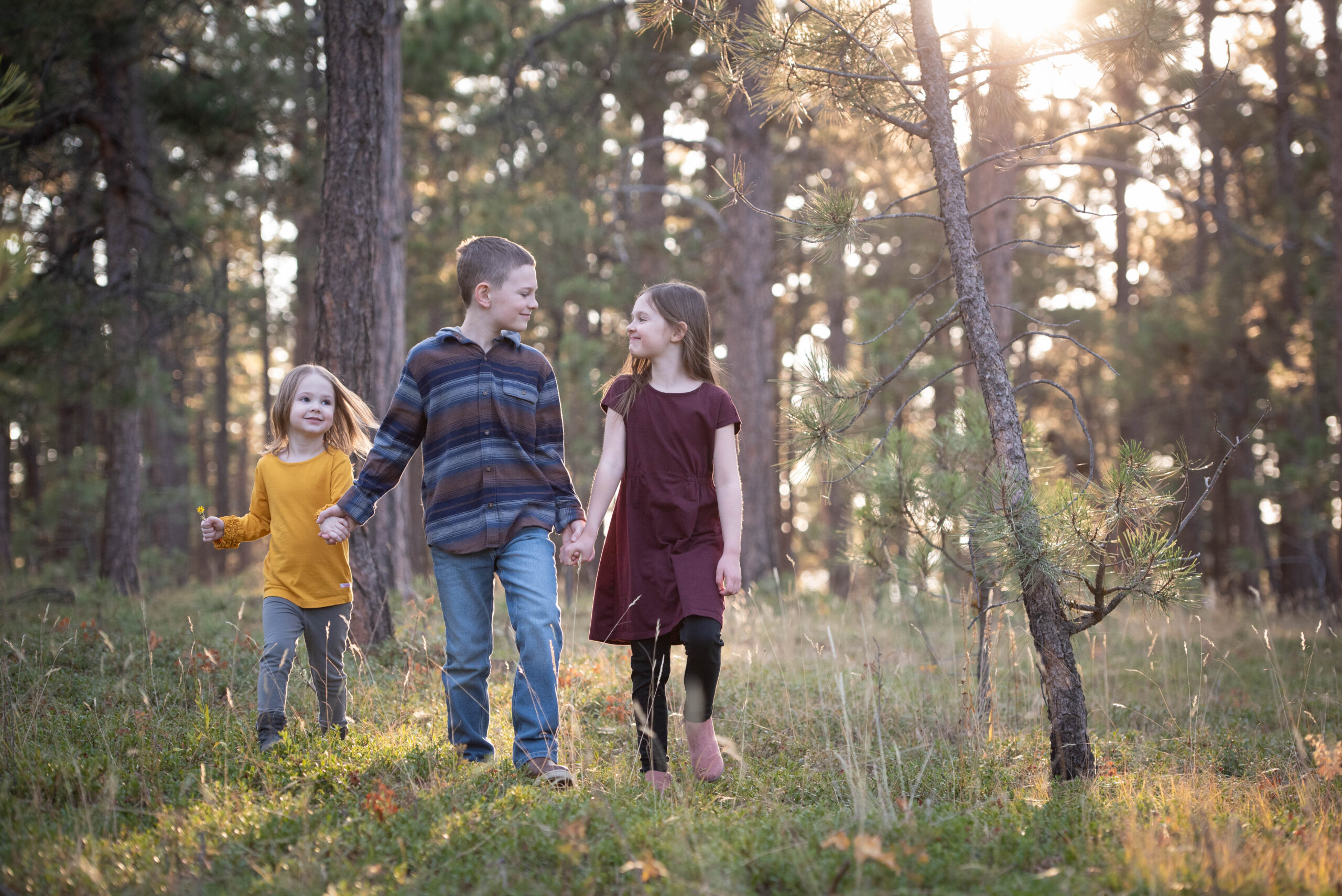 Three young siblings hold hands and walk through some woods Matthews-Vu Medical Group