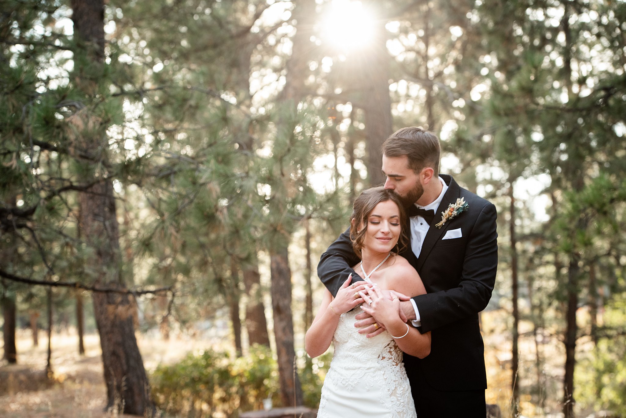 Newlyweds embrace and kiss while standing in a forest at sunset at their black forest wedding venue