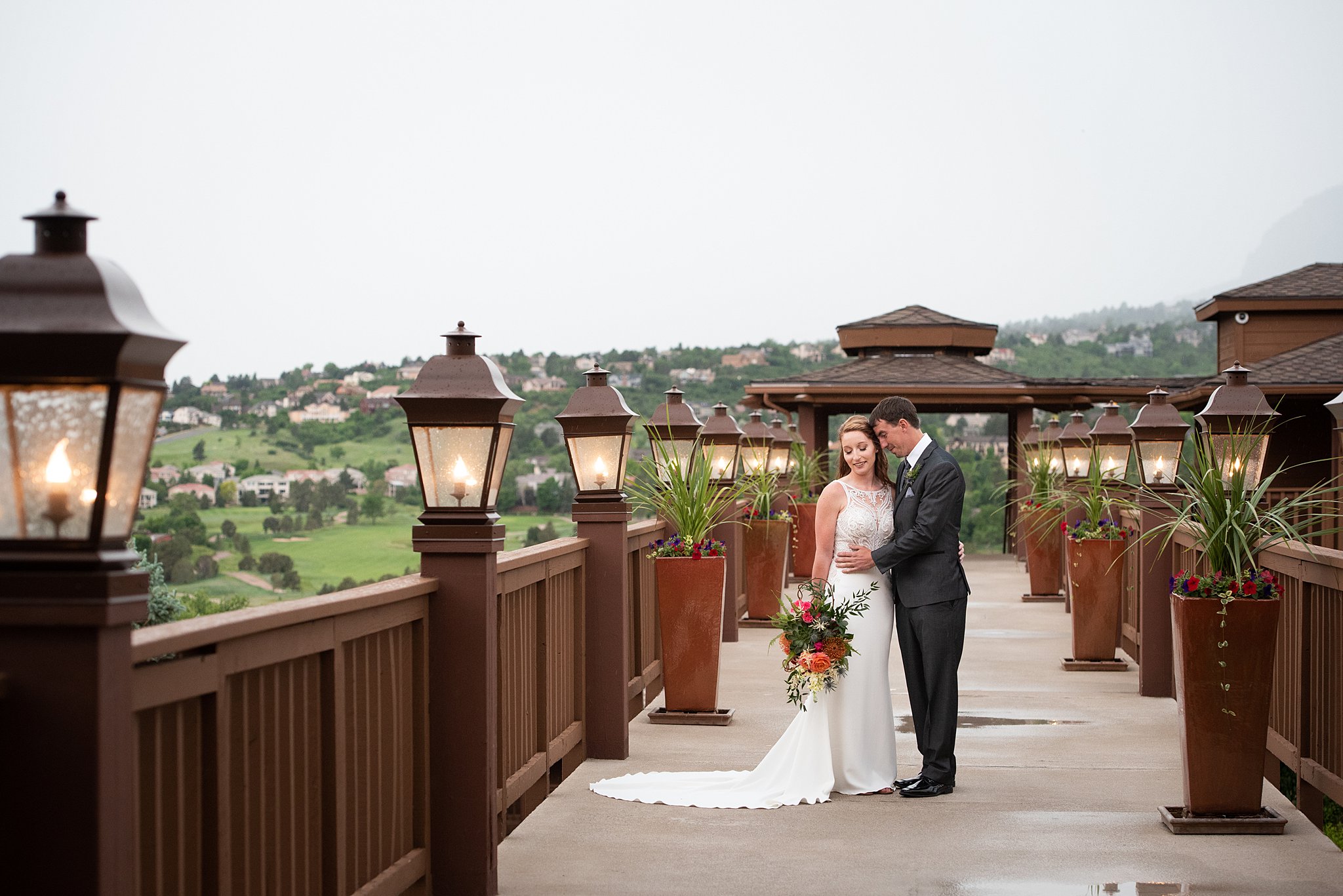 Newlyweds snuggle while standing on a large walkway in the mountains