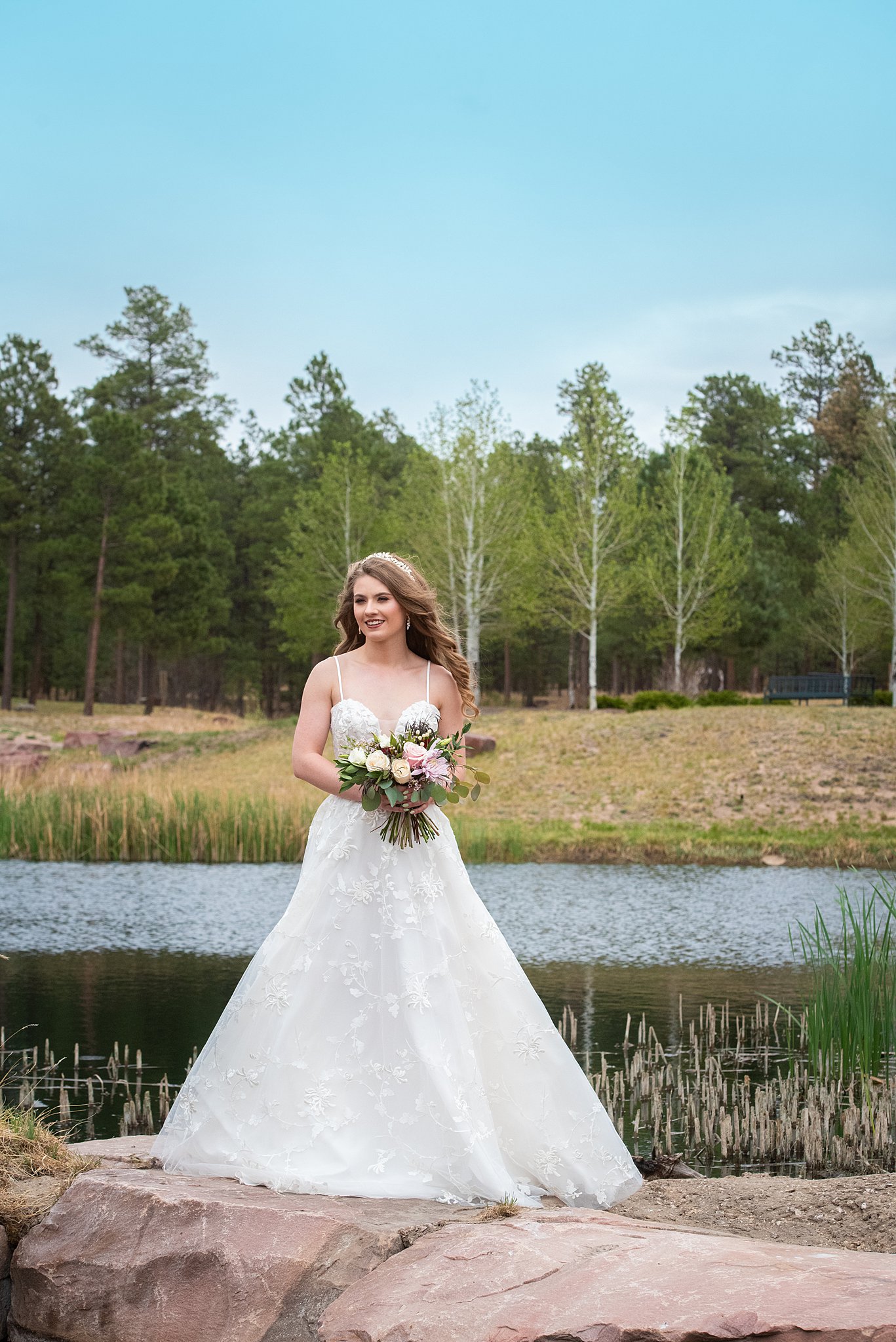 A bride stands on a rock on the edge of a lake holding her bouquet at one of the castle rock wedding venues