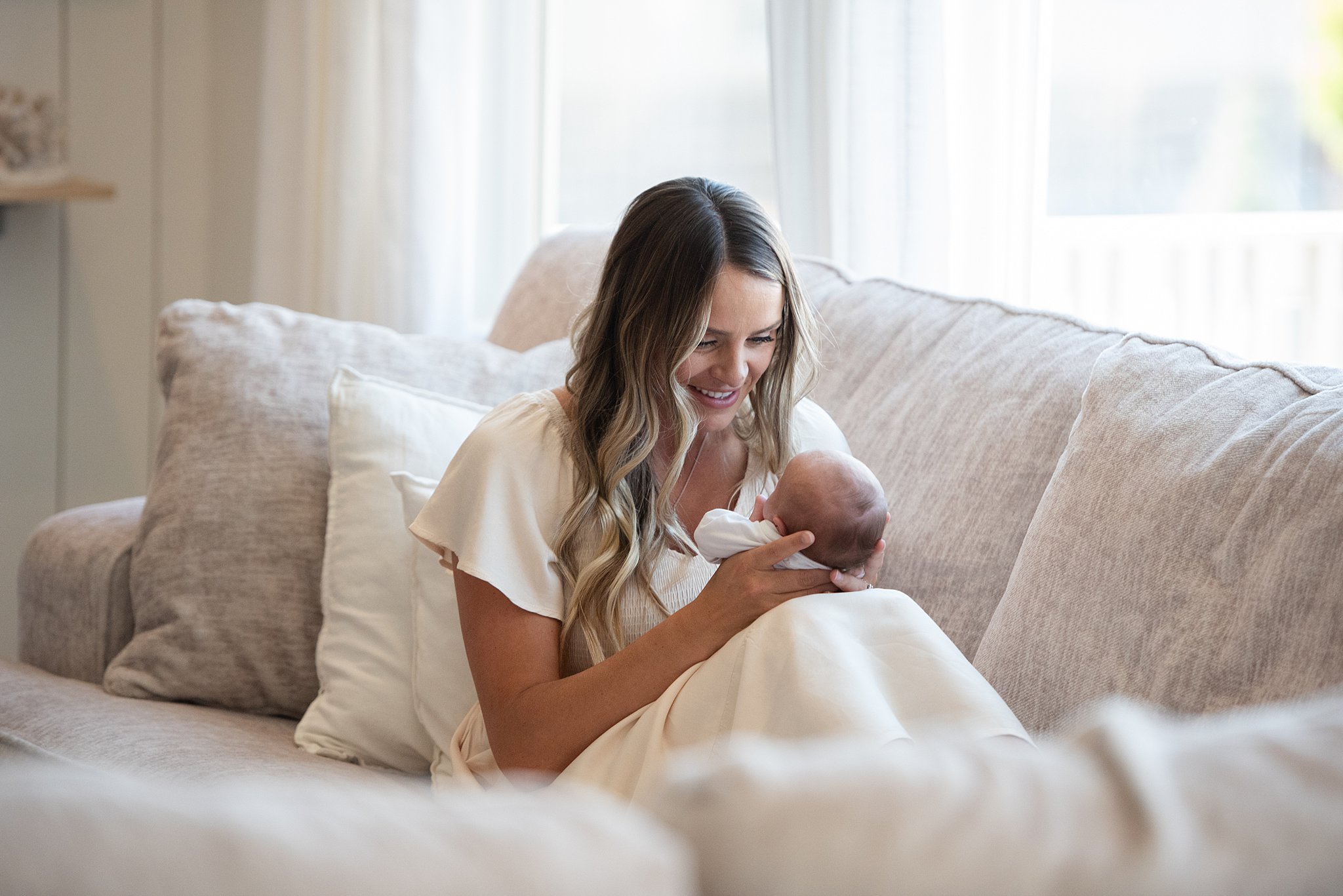 A happy mom holds her newborn baby in her hands while sitting on a couch