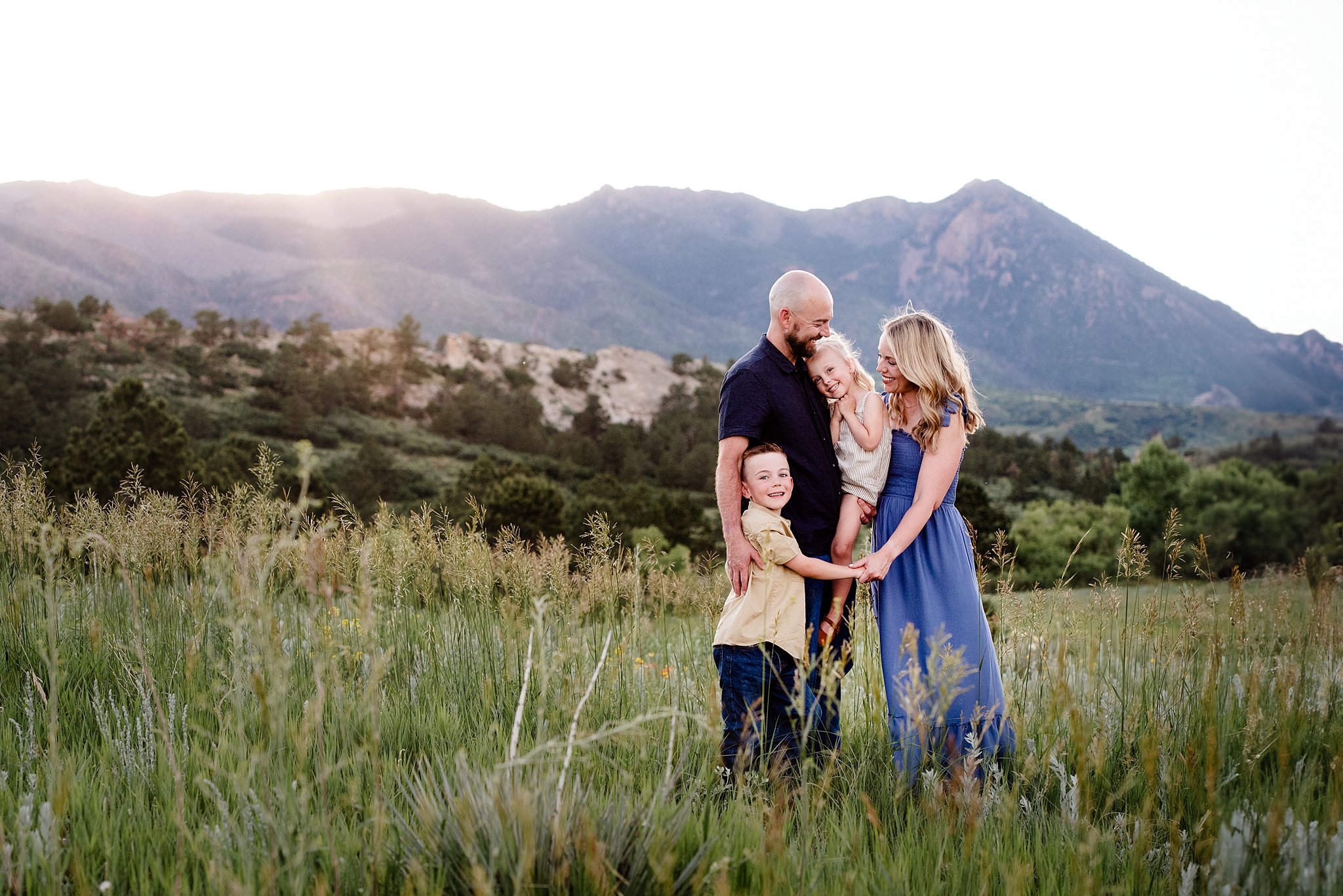 A family of four smile while standing in a pasture at sunset after visiting club pilates colorado springs