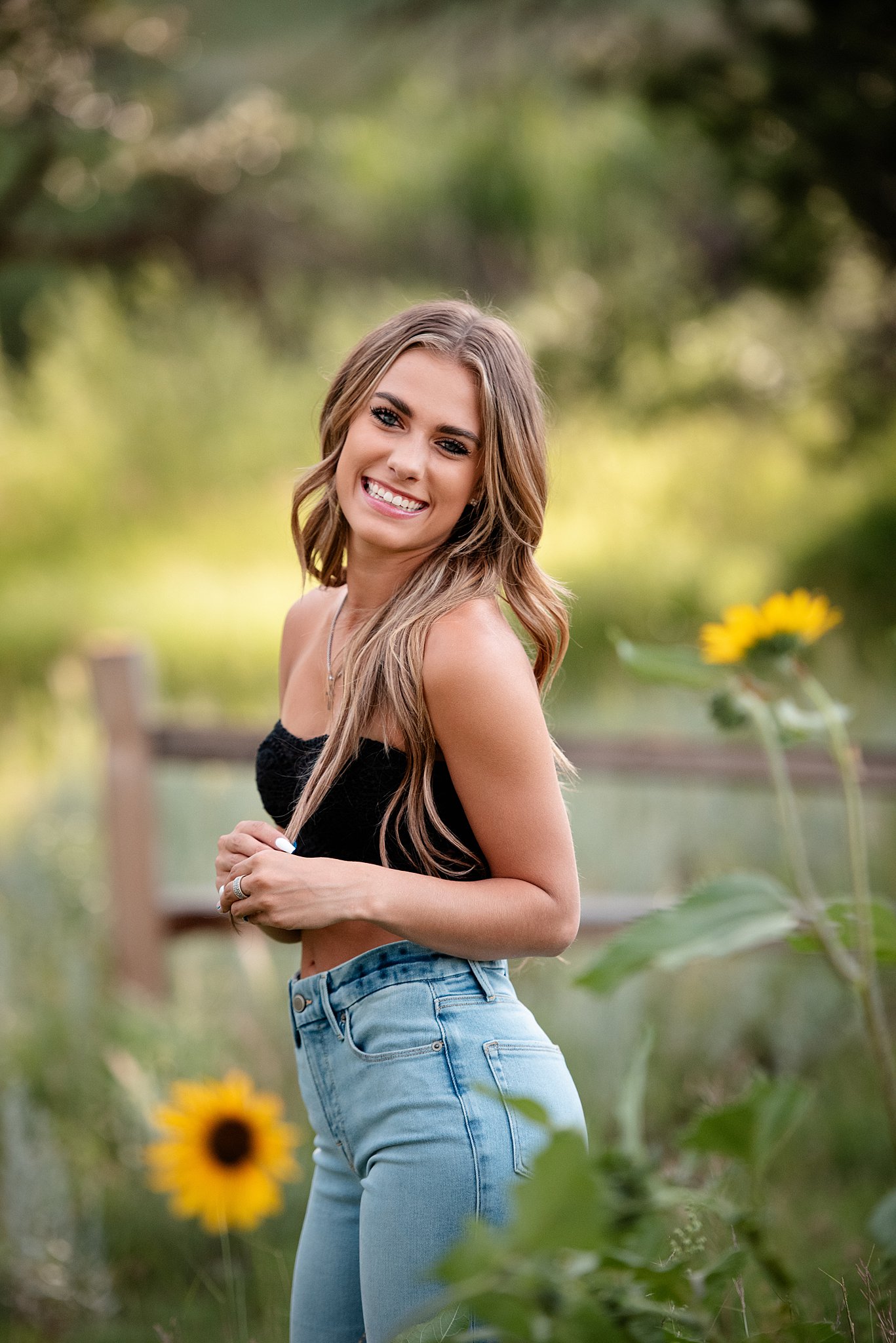 A high school senior smiles over her shoulder while walking through a garden with sunflowers