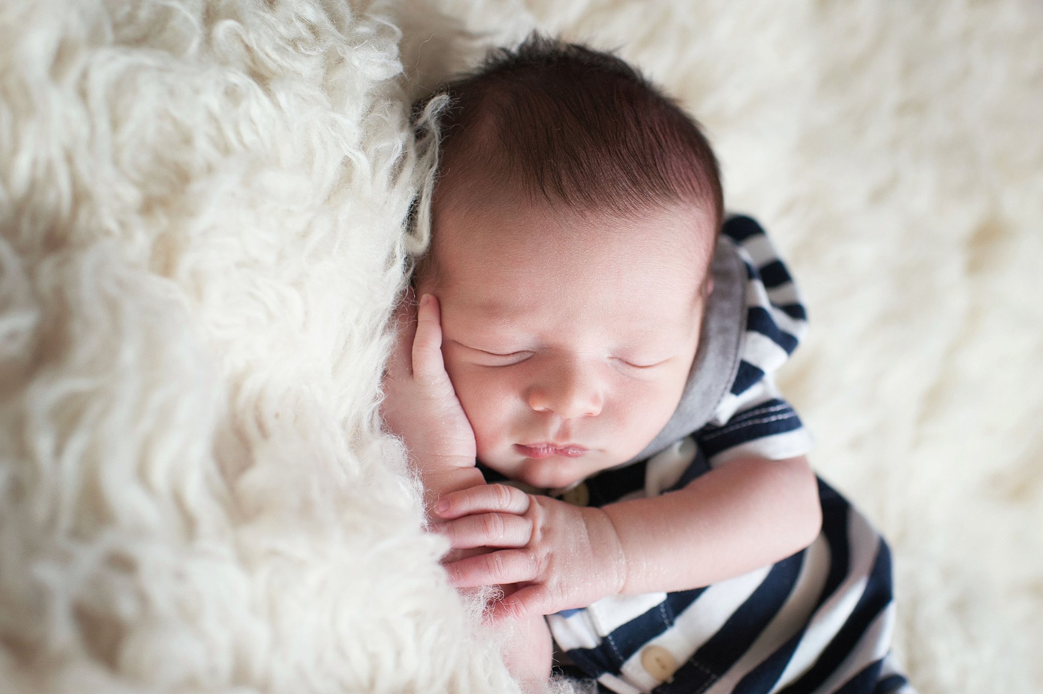 A newborn baby sleeps in a stripe onesie on a fur bed thanks to Colorado Mountain Doulas