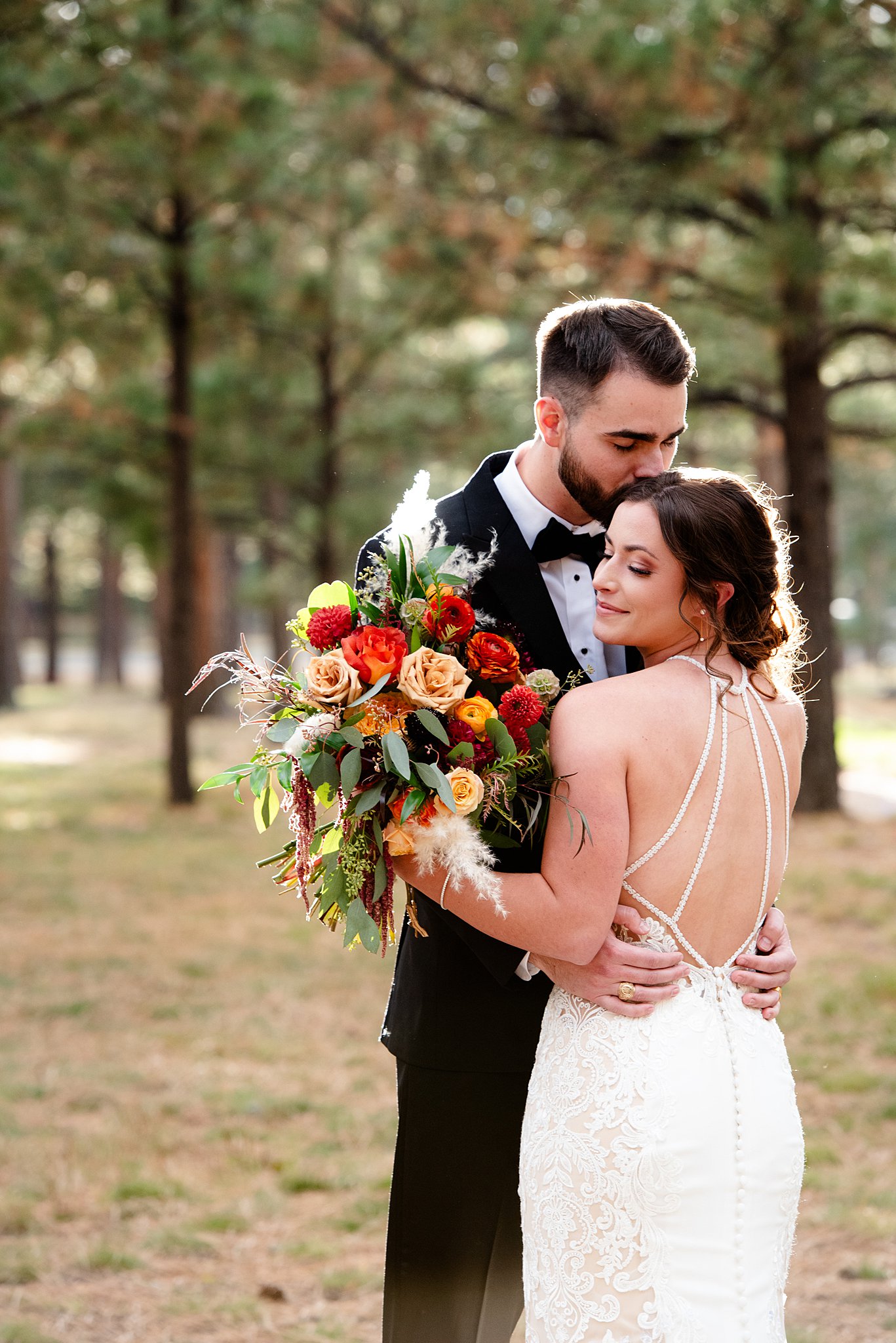 Newlyweds smile and kiss while standing in a forest at sunset at their Colorado Springs Elopement