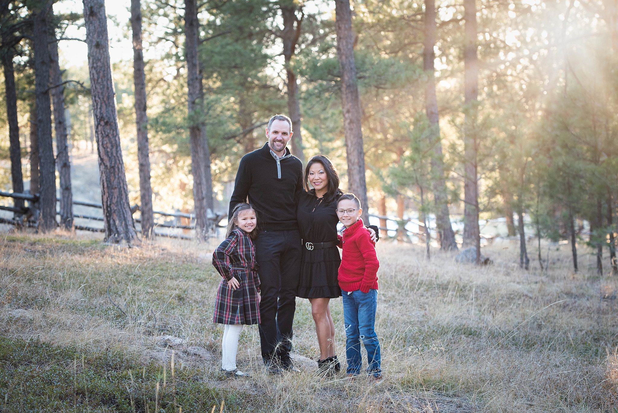 A mom and dad in black stand in a forest park with their young son and daughter at sunset during colorado springs family activities