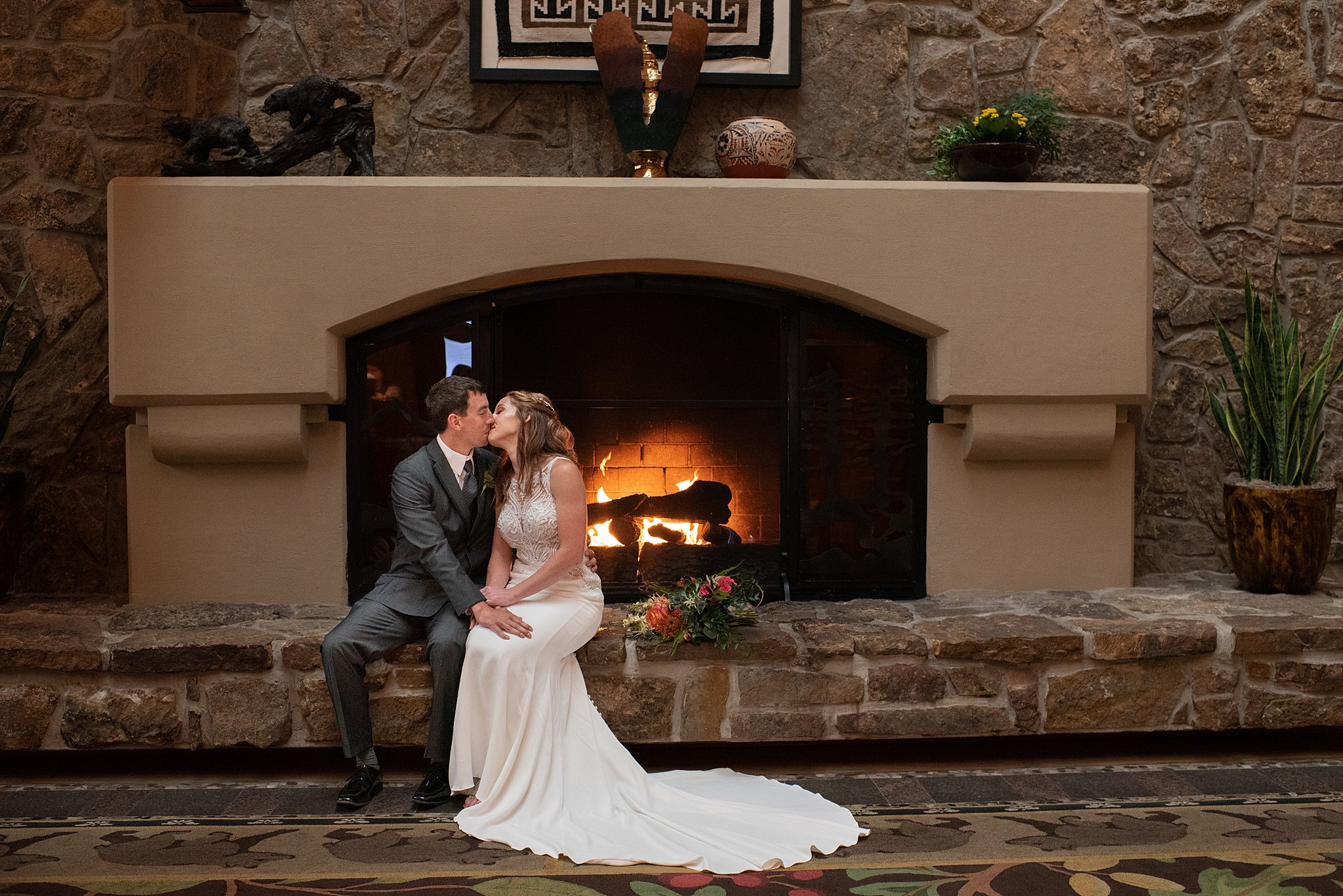 Newlyweds sit on the edge of a large stone fireplace and kiss at one of the Colorado Springs Wedding Venues