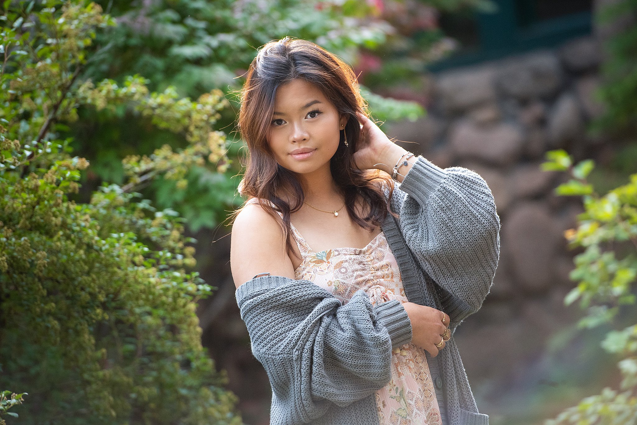 A high school senior in a large grey sweater and tan dress stands in a garden with a hand in her hair after applying for university of colorado colorado springs scholarships