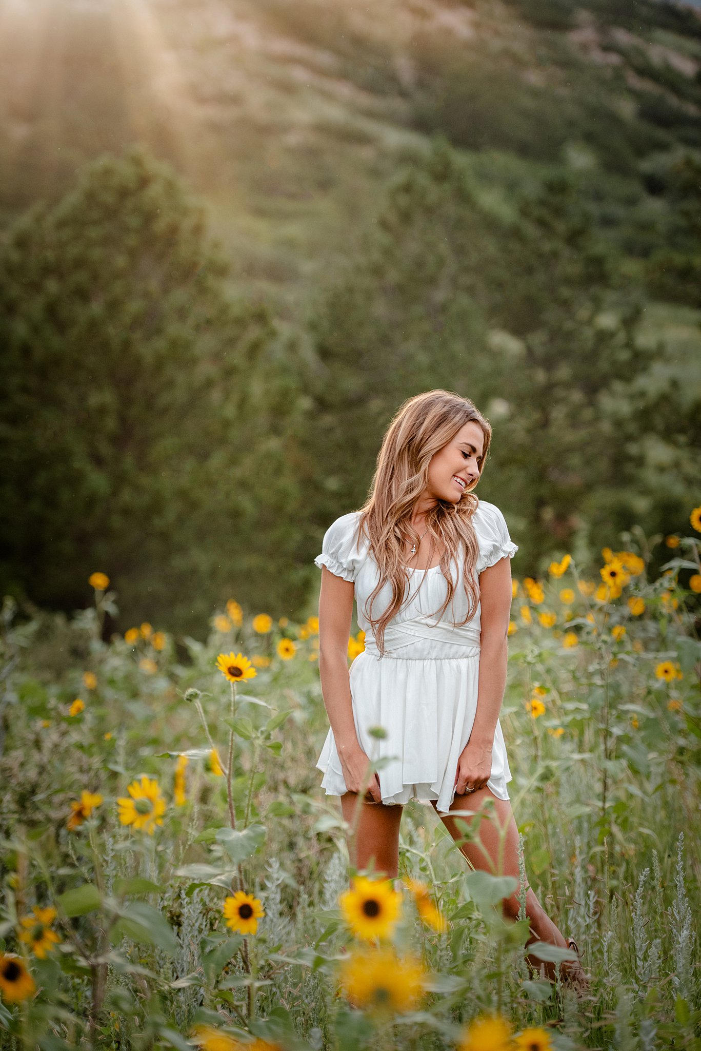 A high school senior in a white dress stands in a field of wildflowers at sunset
