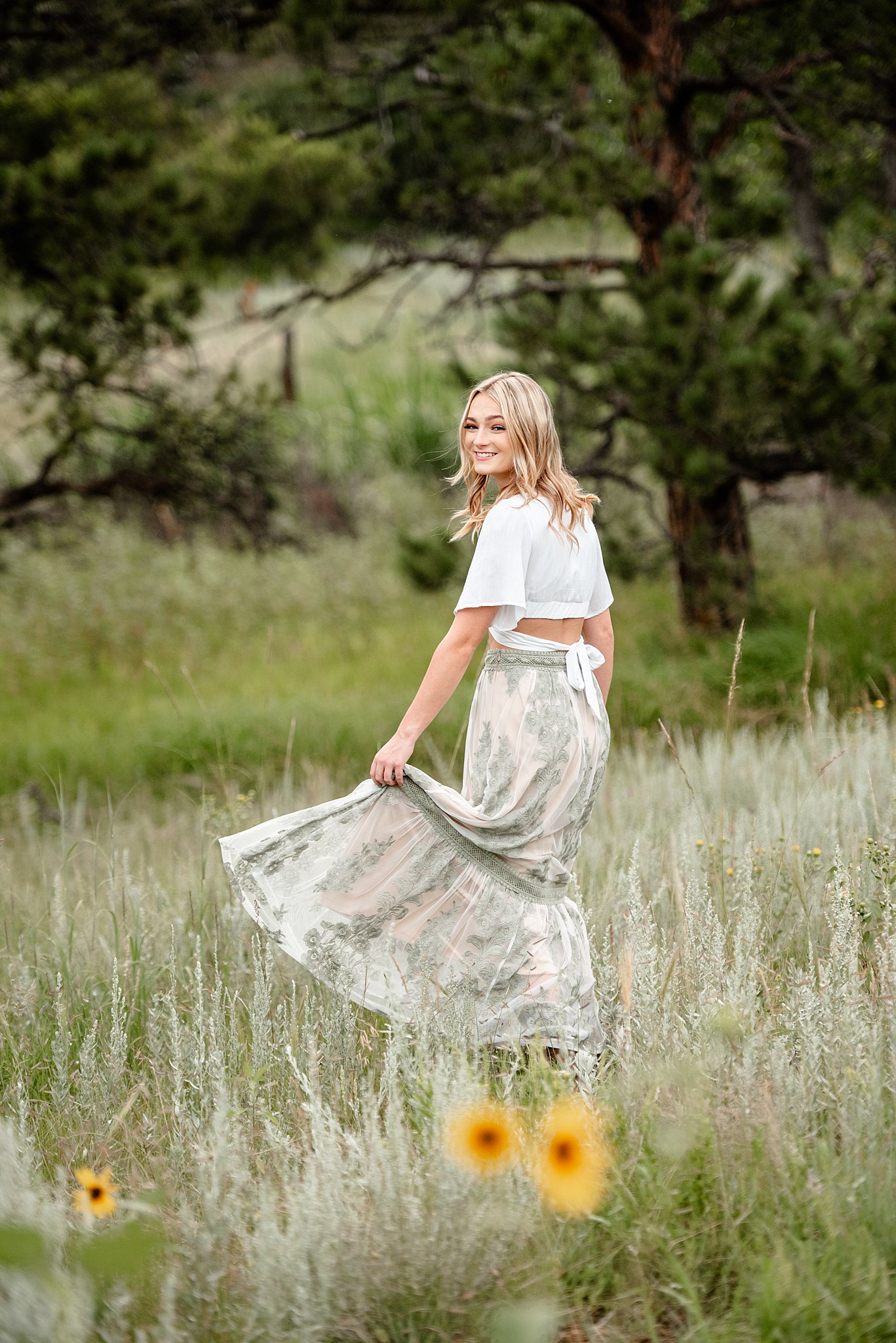 A high school senior in a flowy dress walks through a field with wildflowers at ute valley park