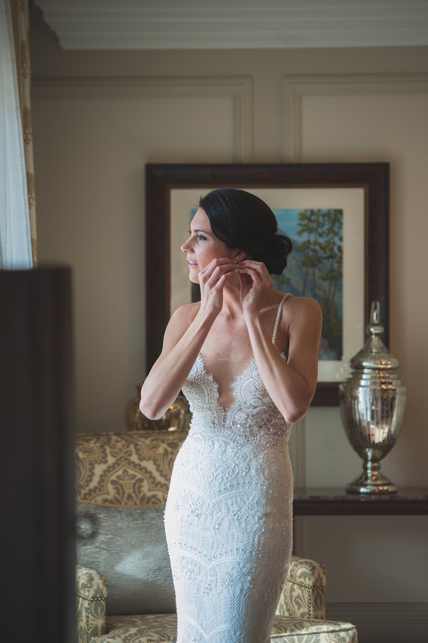 A bride puts on her earrings in a lace dress for her Wine and Nosh wedding