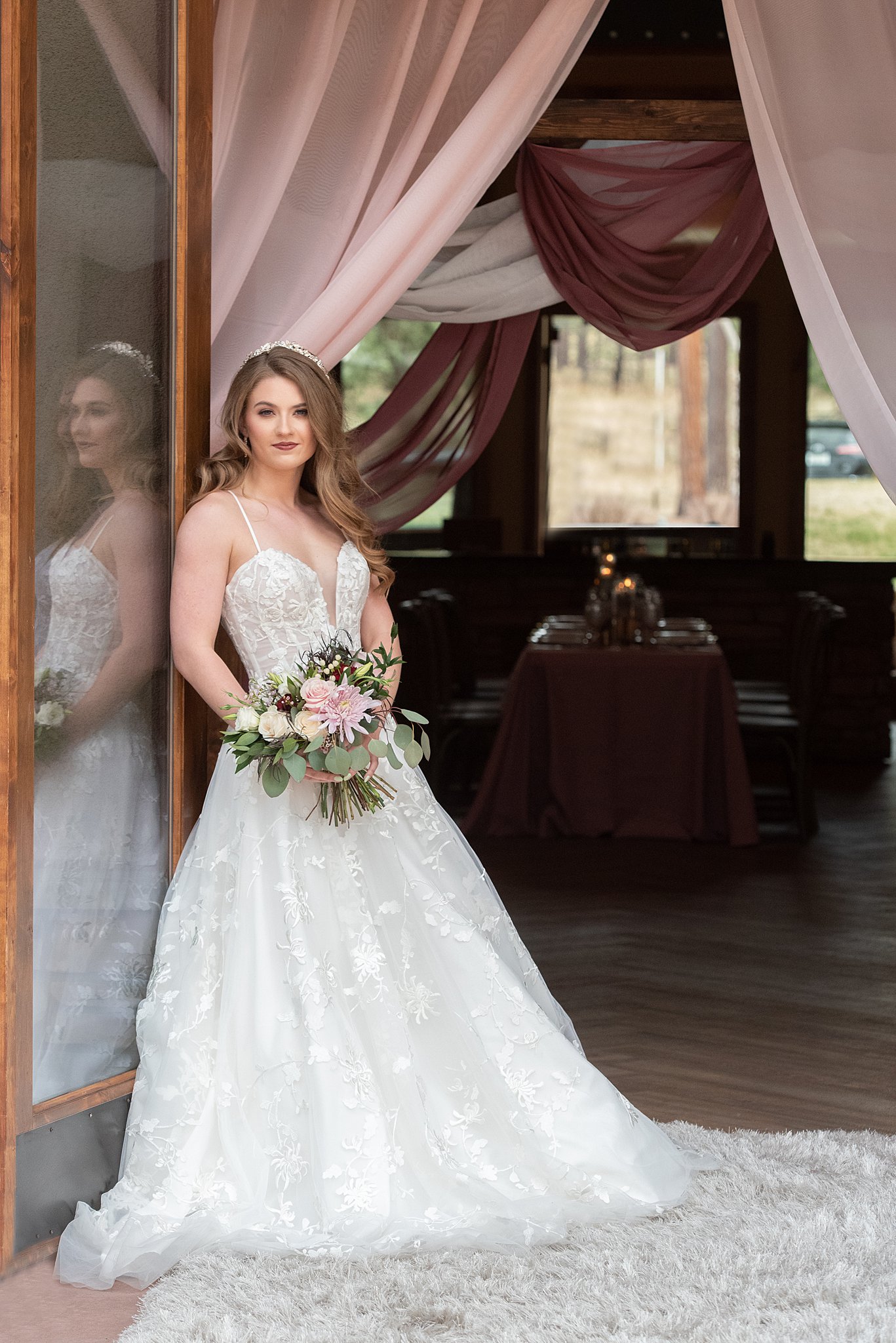 A bride stands in a doorway in a lace dress holding her bouquet