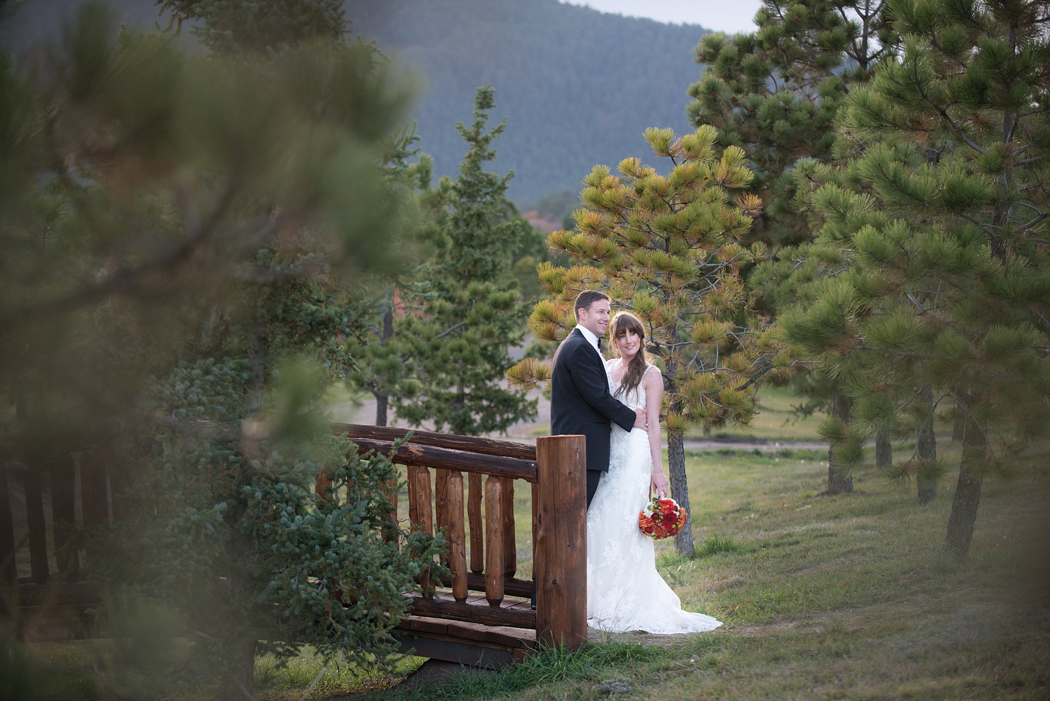 Newlyweds stand on a wooden log bridge hugging in a forest at Wine and Nosh