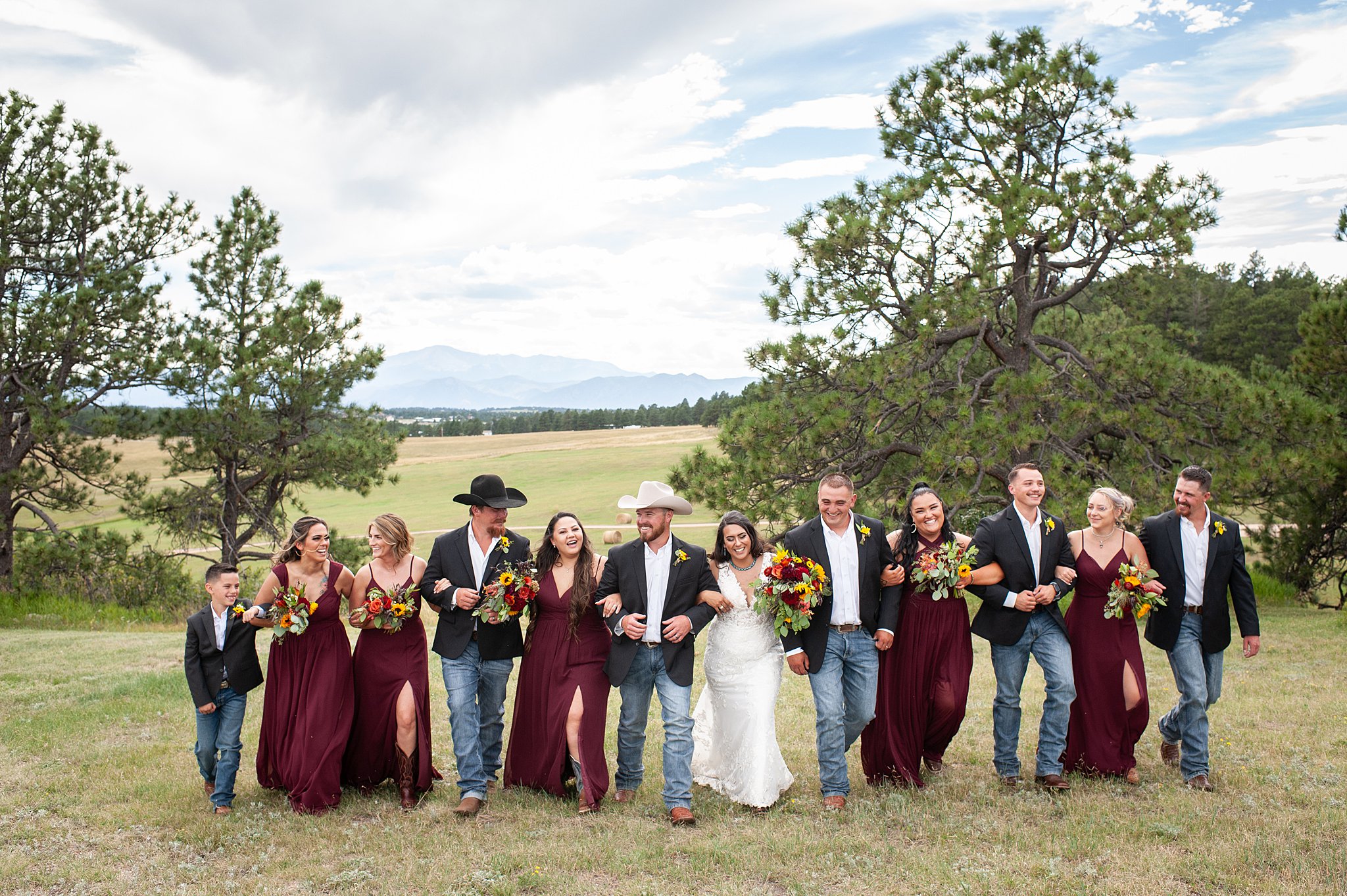 Newlyweds walk arm in arm with their wedding party through a pasture