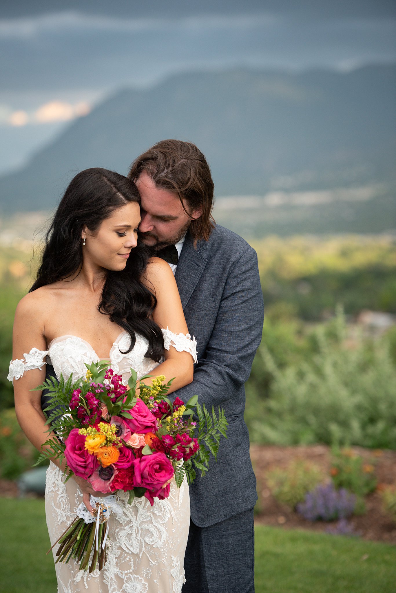 A bride and groom snuggle in a garden at their Garden Of The Gods Club Wedding with a colorful bouquet