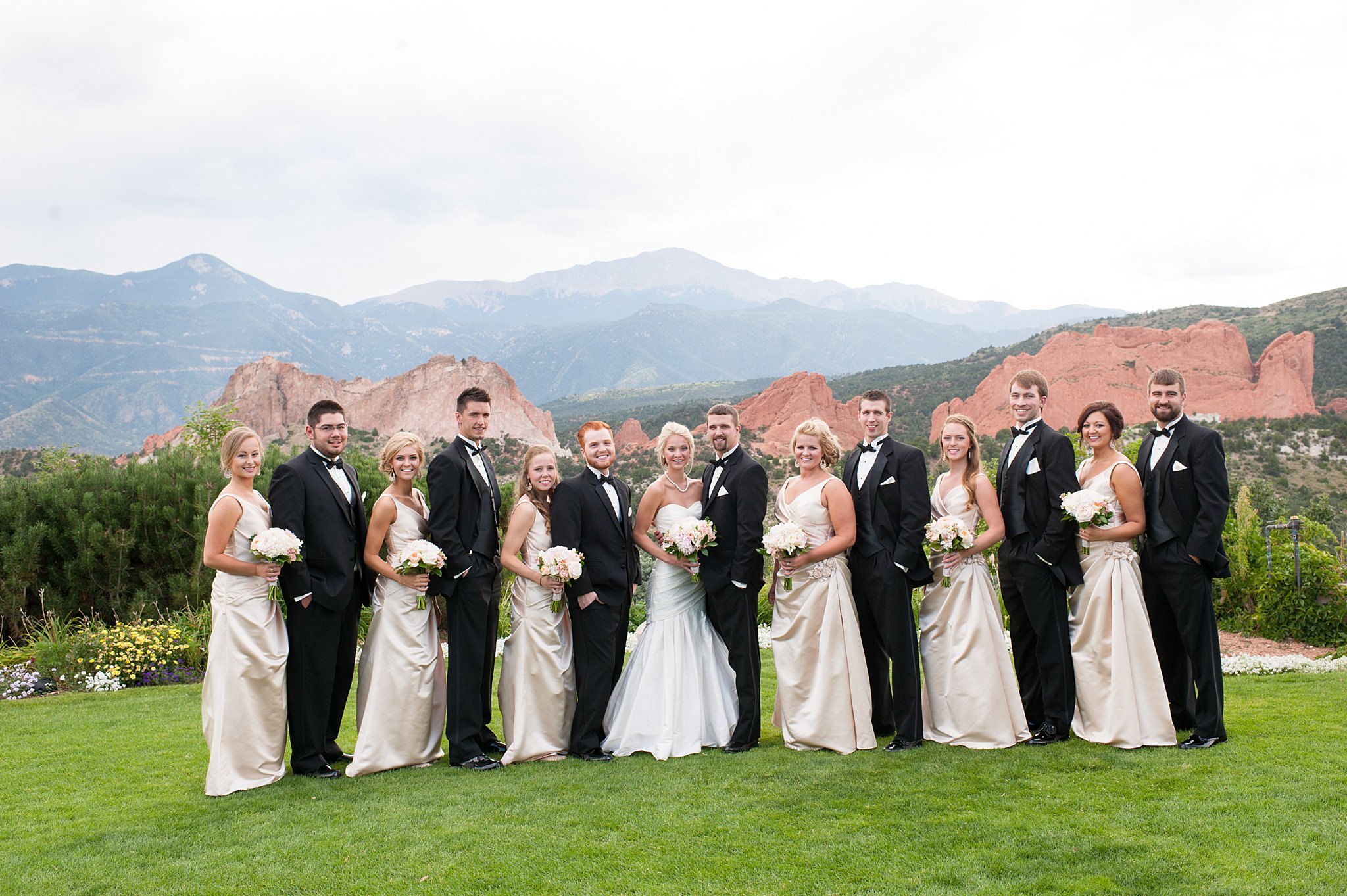 A bride and groom smile while standing in the grass with their wedding party