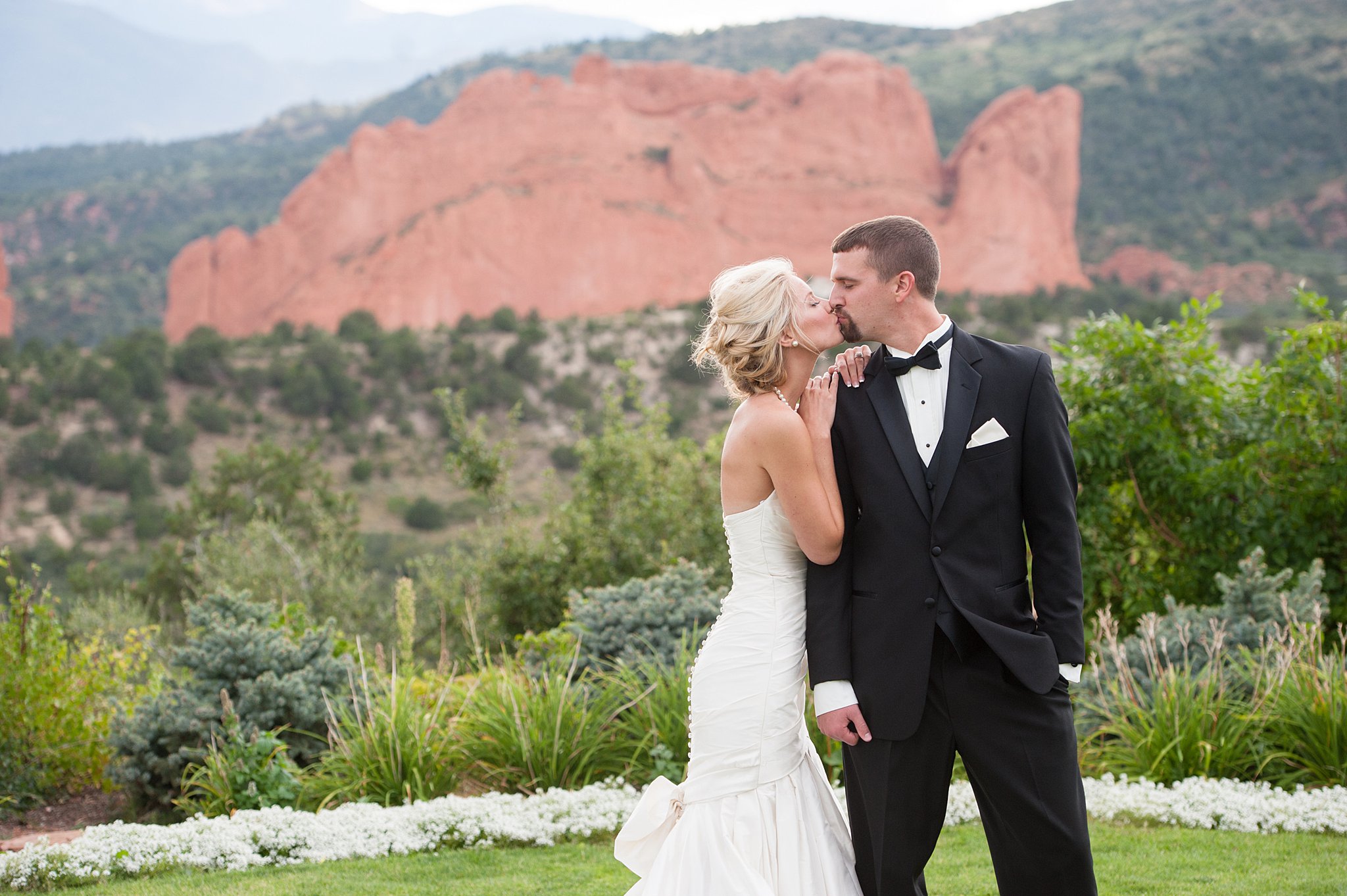 Newlyweds kiss while walking the garden lawn at their Garden Of The Gods Club Wedding