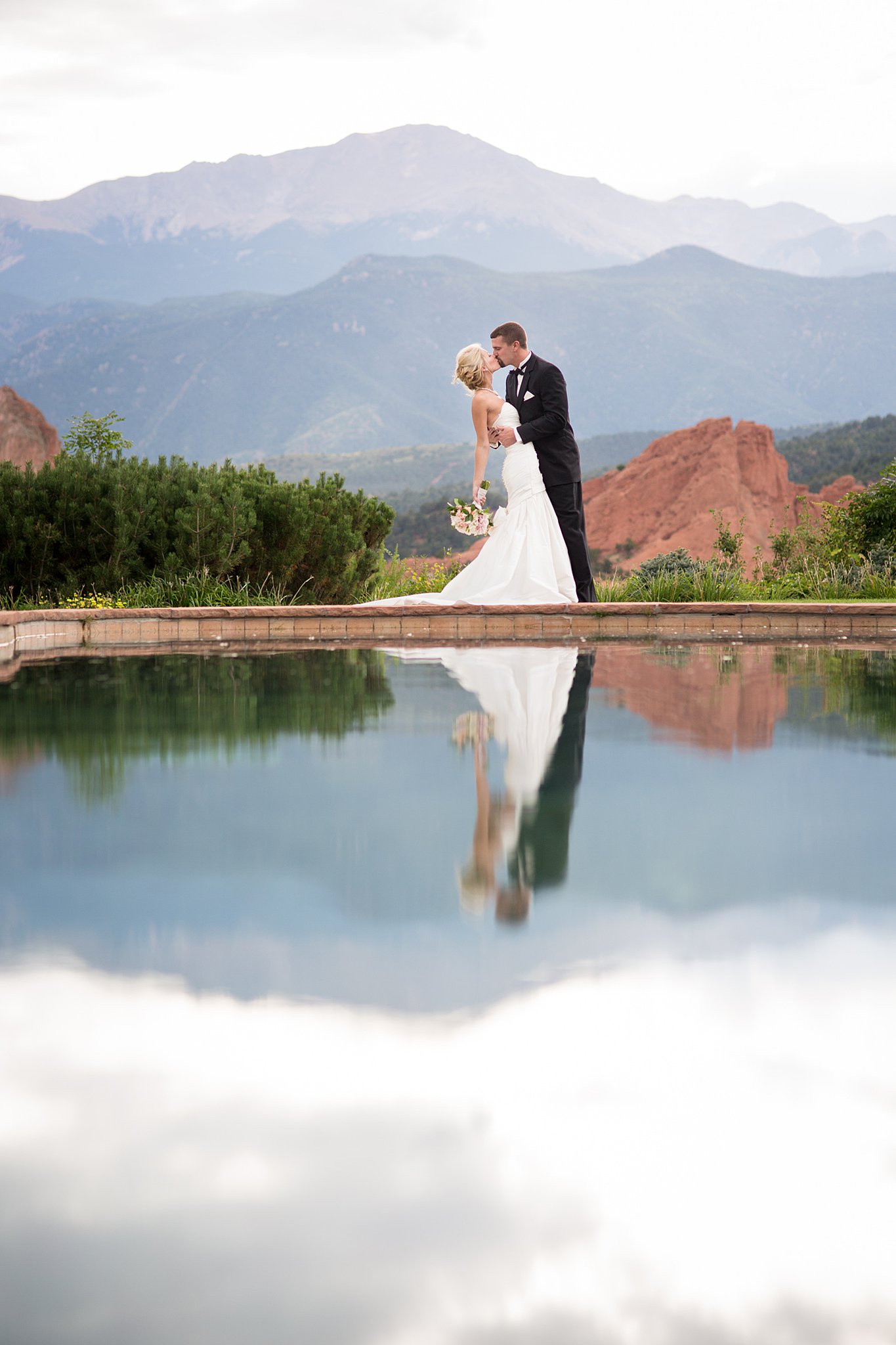 Newlyweds kiss on the edge of a pool at their mountain wedding