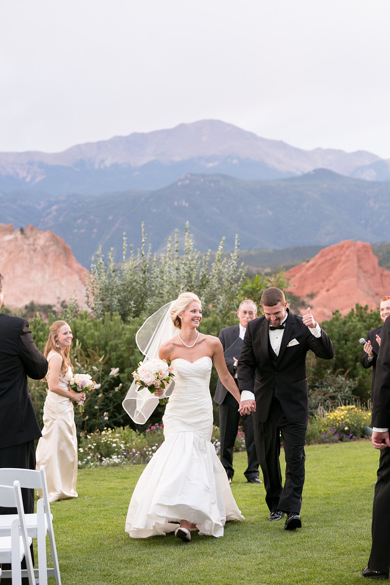 Newlyweds hold hands and smile while exiting their Garden Of The Gods Club Wedding ceremony on the lawn