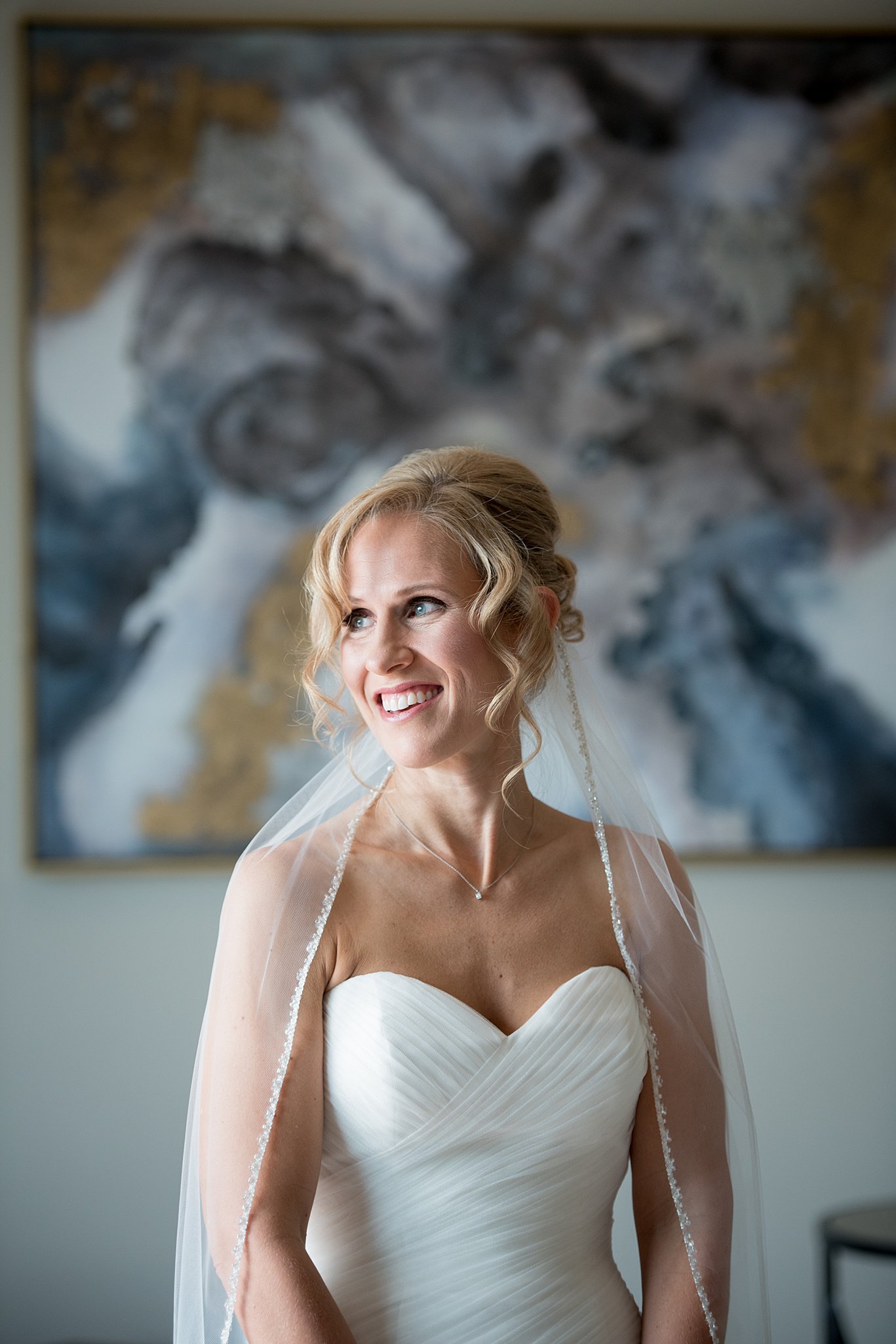 A happy bride smiles while standing indoors in her dress and veil