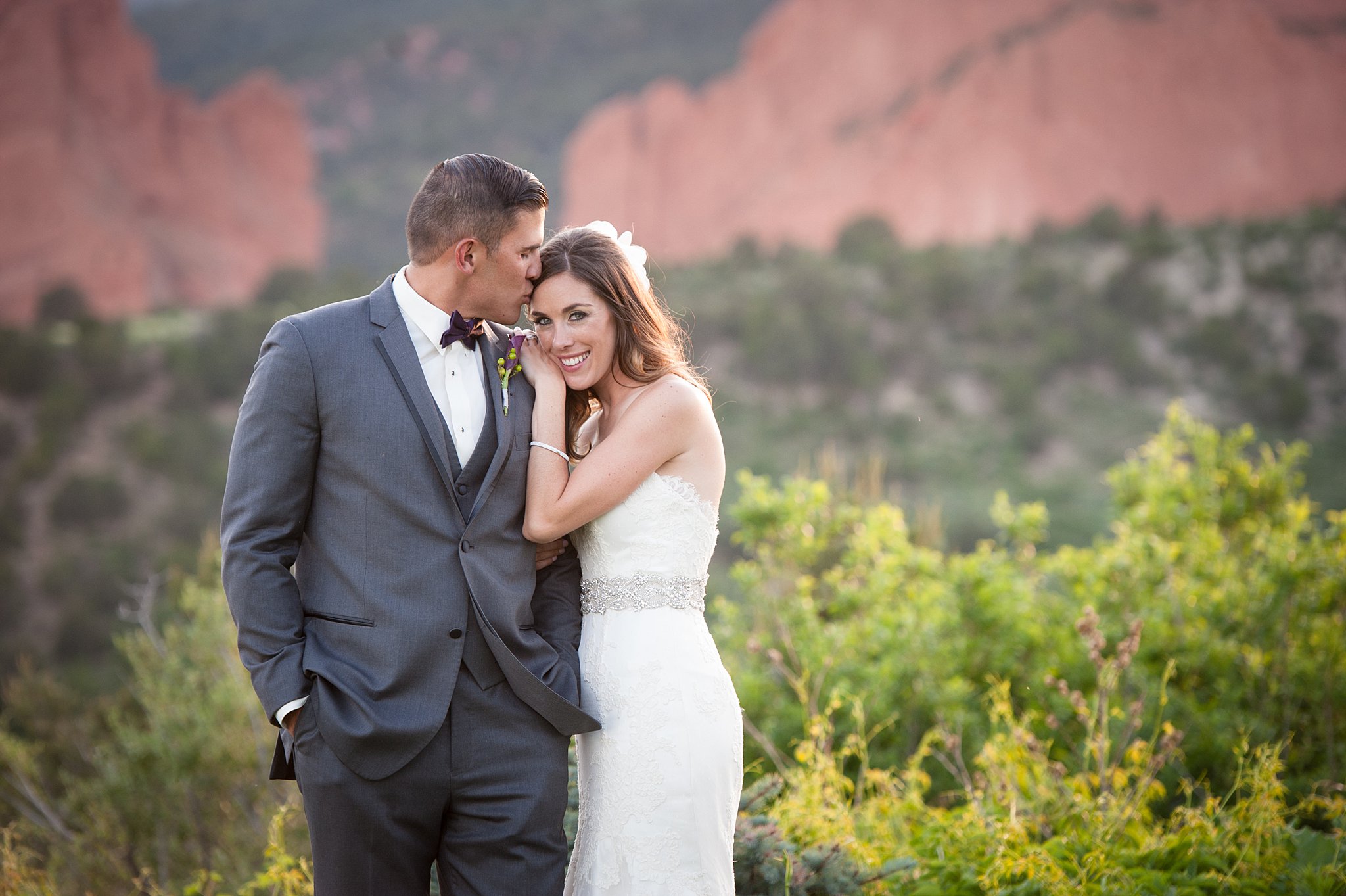 A bride smiles while leaning on her groom's shoulder as he kisses her head