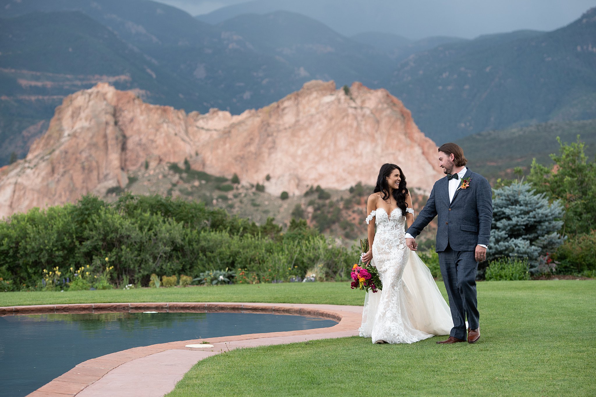 Newlyweds walk around the pool in the lawn laughing and holding hands