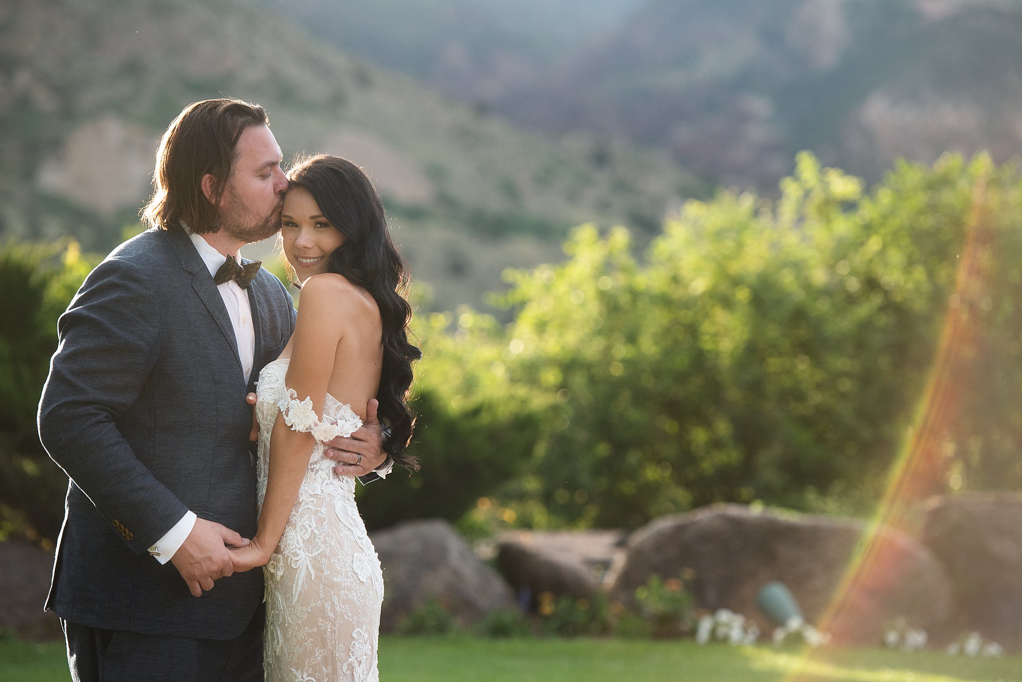 A groom kisses his happy bride on the head as they snuggle at sunset