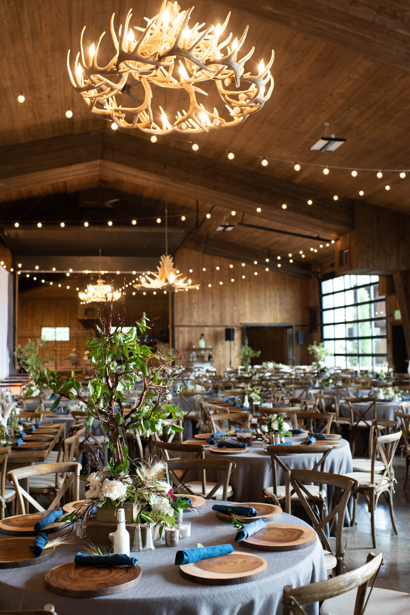 A wedding reception set up under antler chandeliers with grey linen and wooden chargers