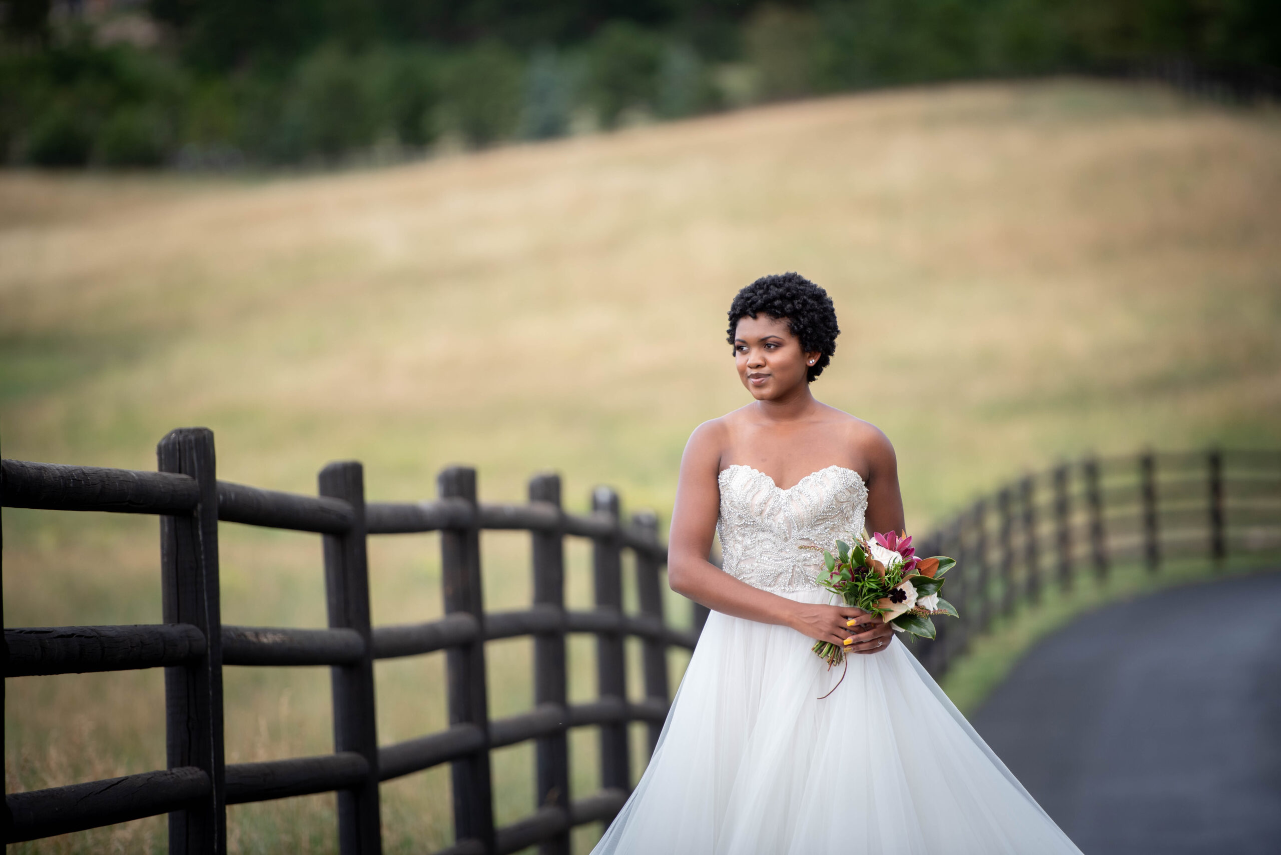 A bride smiles while walking on a sidewalk along a pasture fence