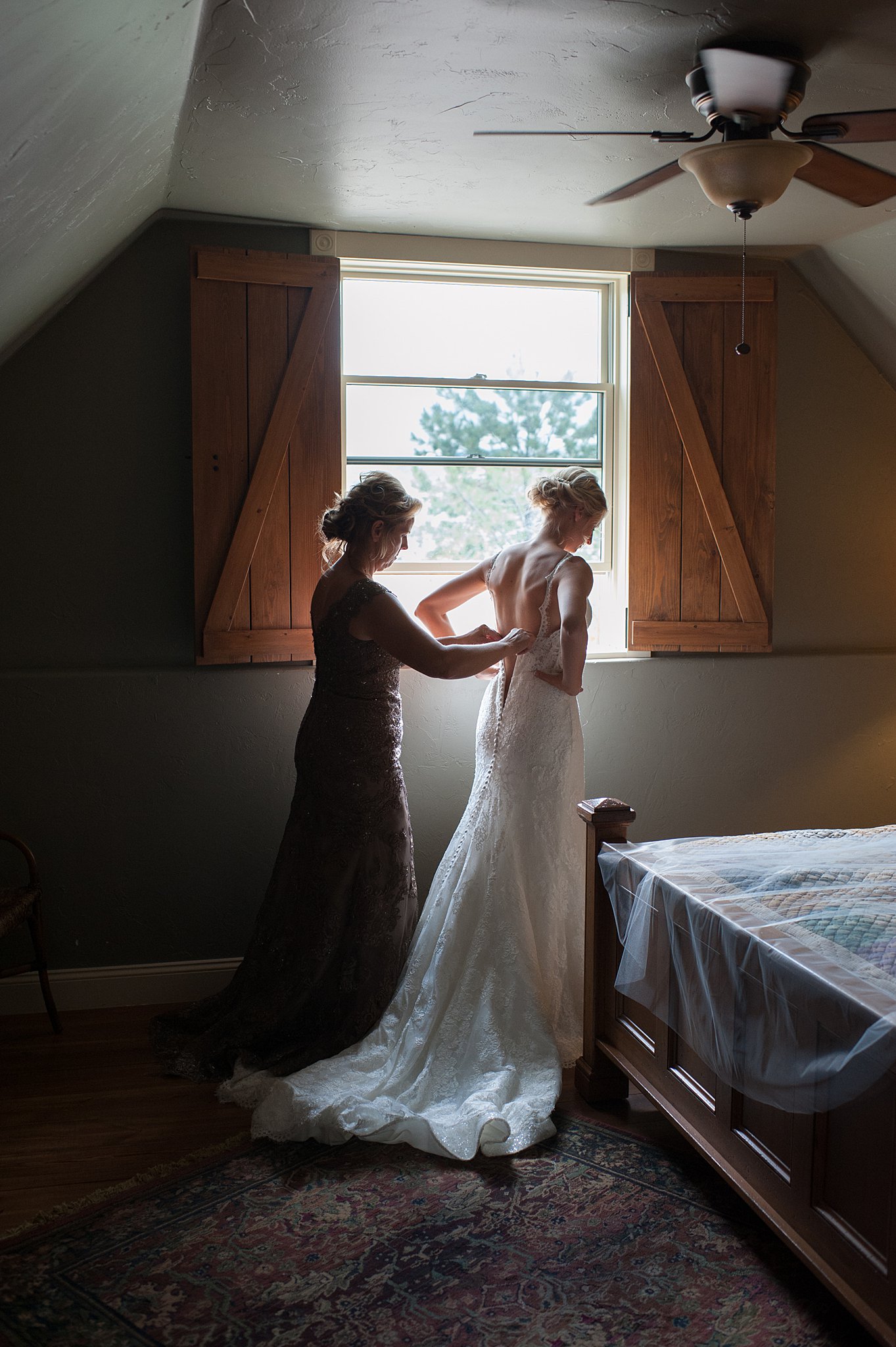 Mom helps a bride into her dress in a bedroom under a window