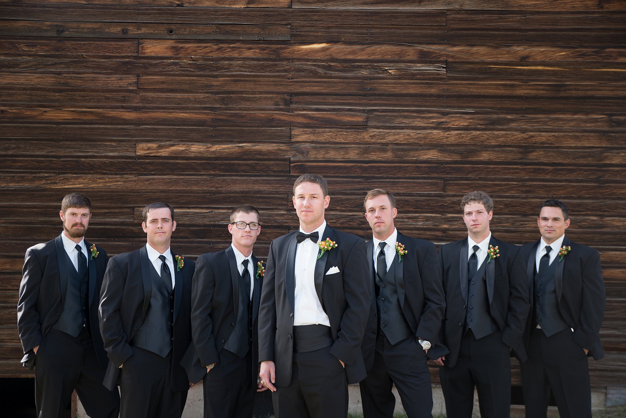 A groom stands with his groomsmen in all black suits with hands in pockets at his Spruce Mountain Ranch wedding