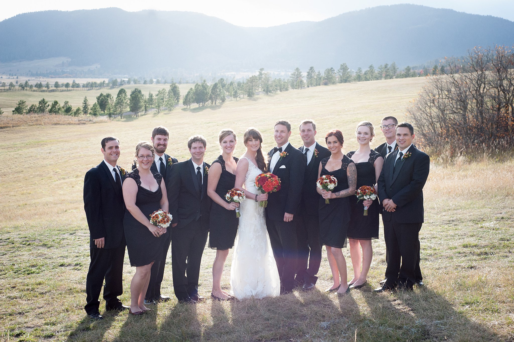 Newlyweds smile while standing with their wedding party in a meadow at their Spruce Mountain Ranch wedding