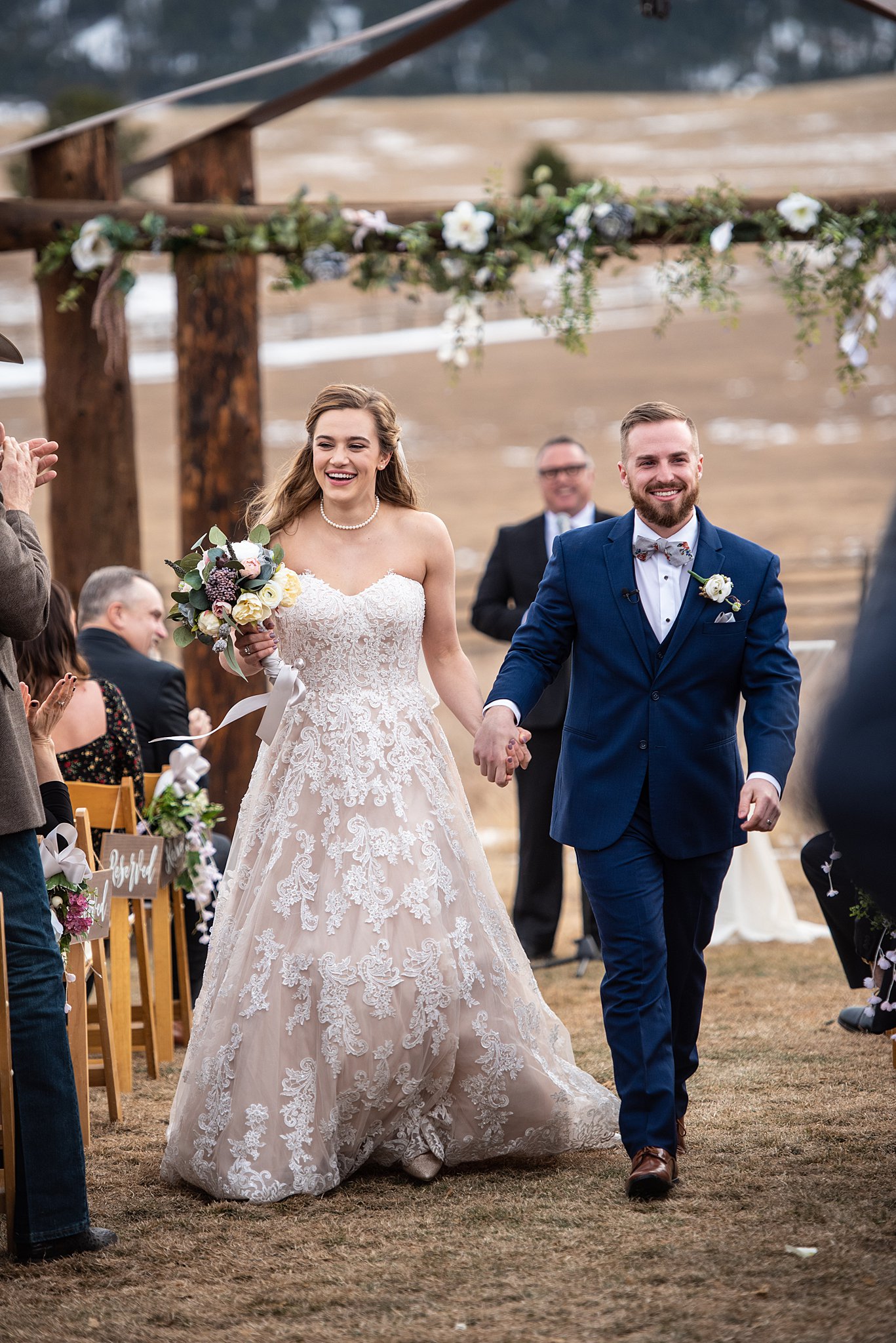 A bride and groom smile while walking up the aisle holding hands after their Spruce Mountain Ranch wedding ceremony