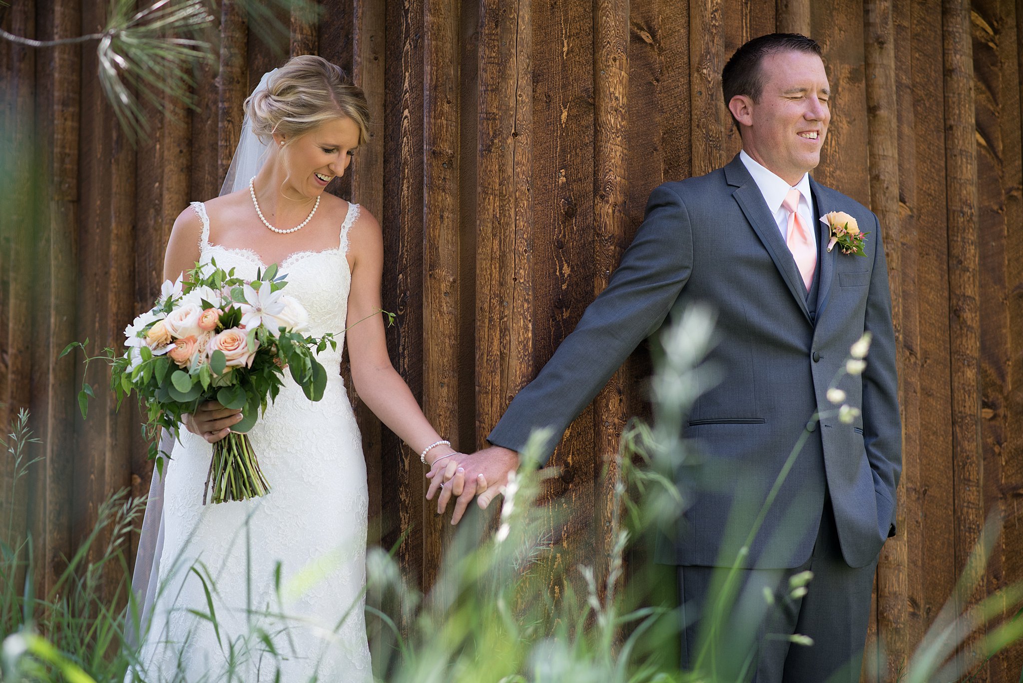 Newlyweds hold hands around a corner for their first touch with big smiles