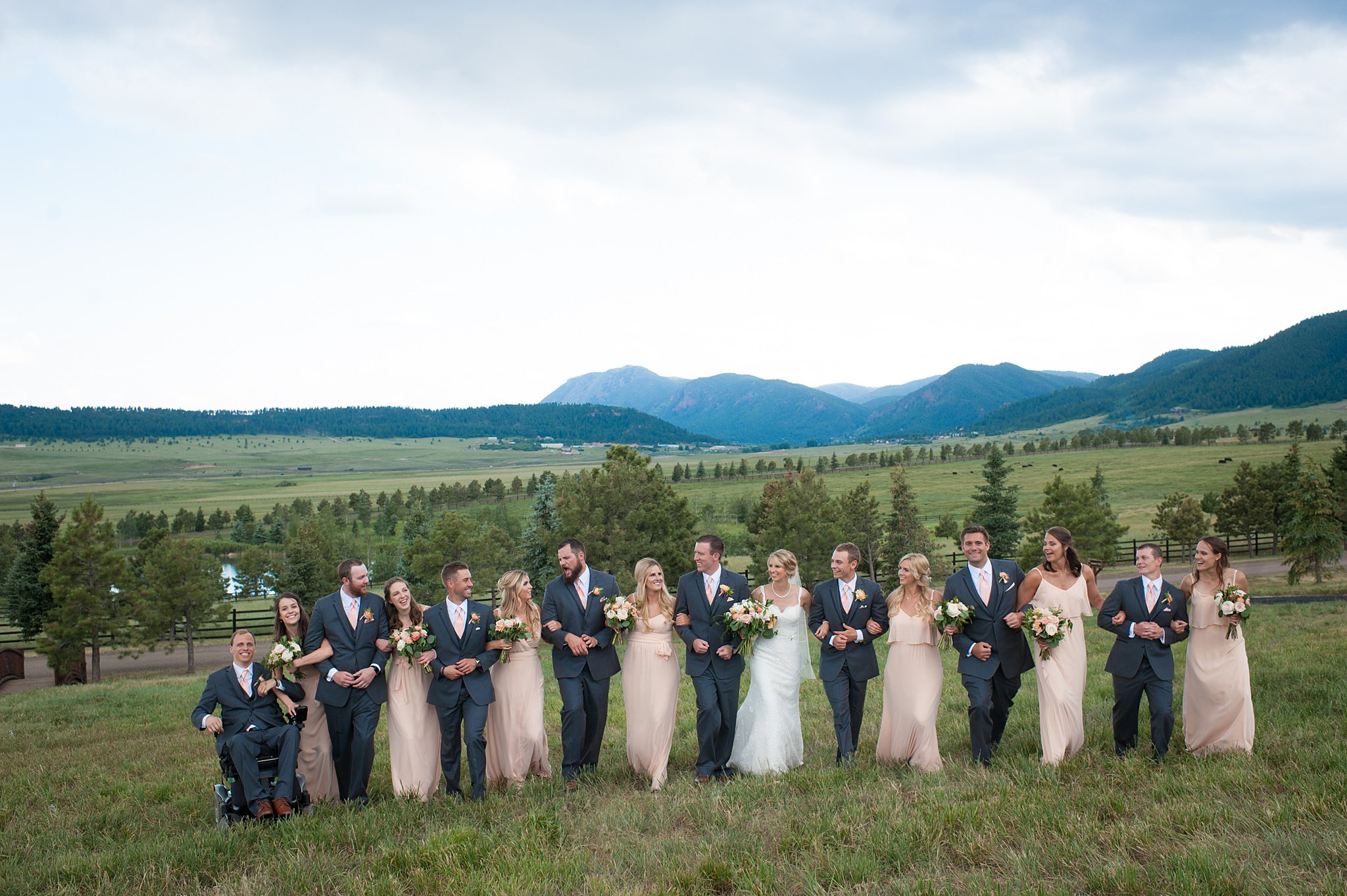 Newlyweds lock arms and walk in a pasture with their large wedding party