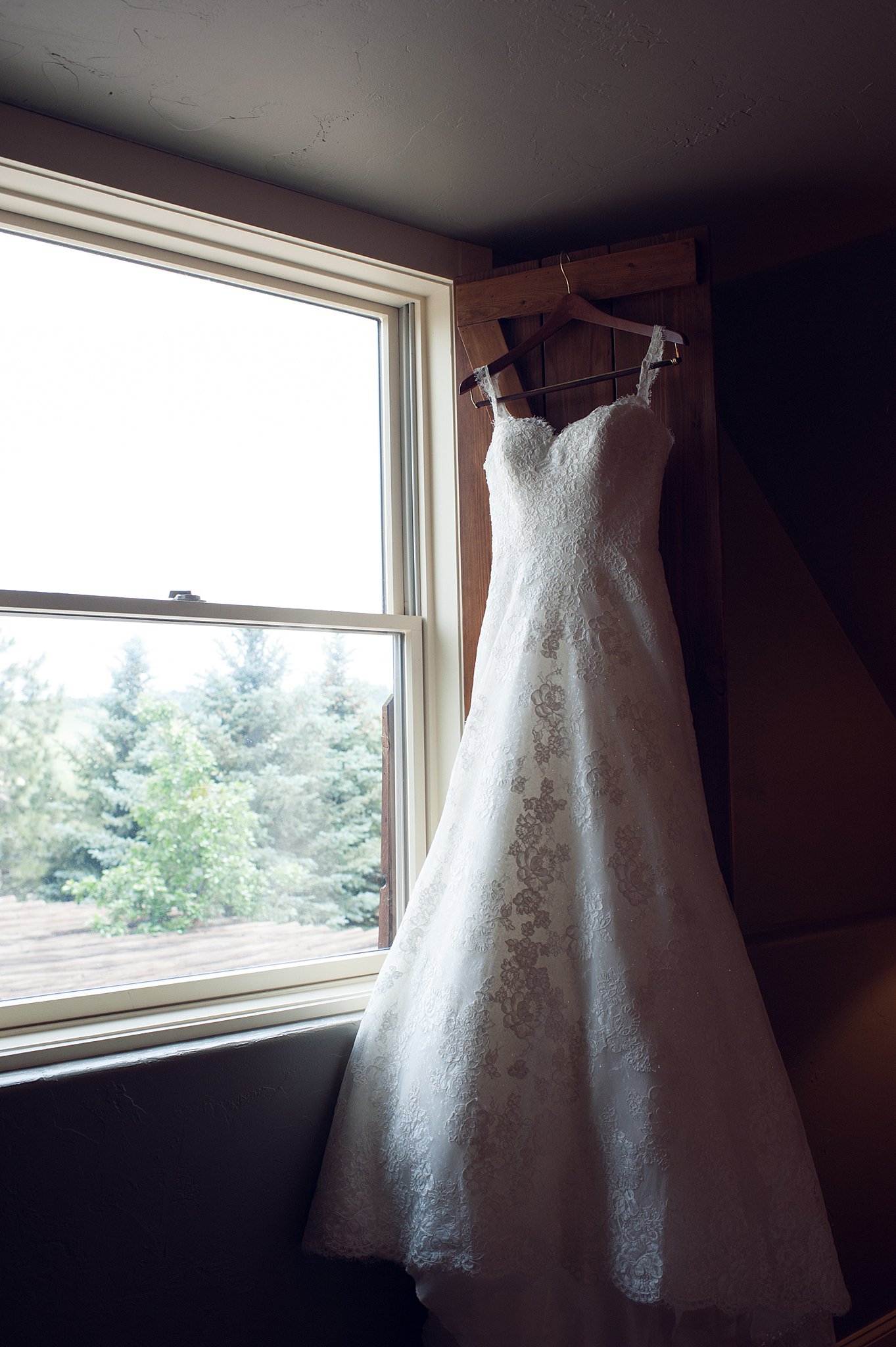 A brides lace embroidered dress hangs on a window shutter