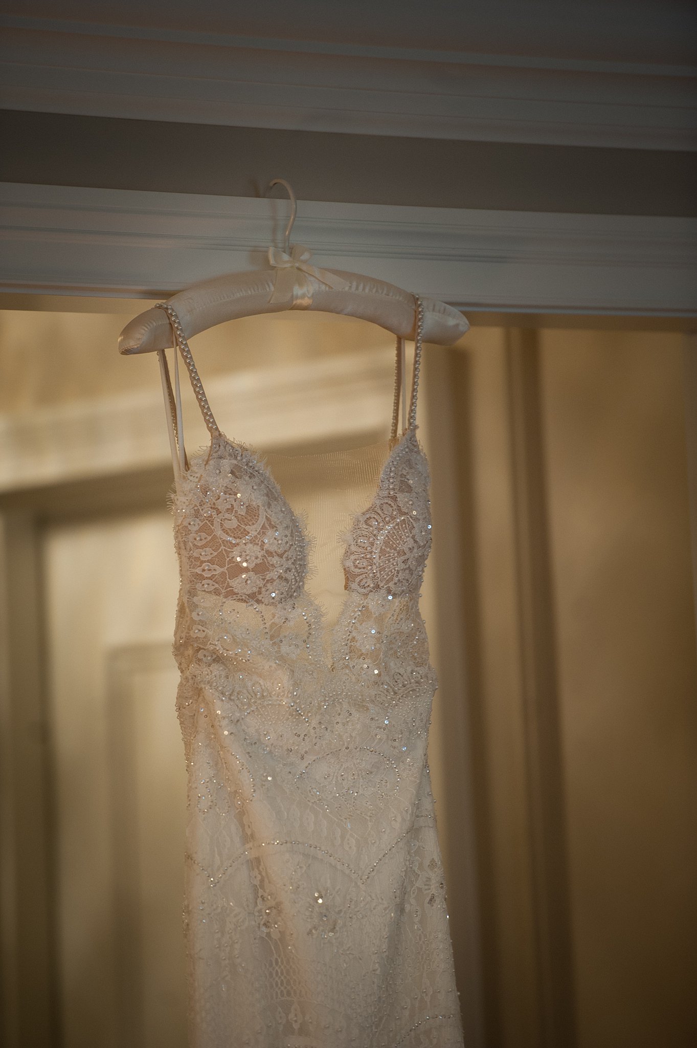 Details of a bride's lace dress hanging in a door frame