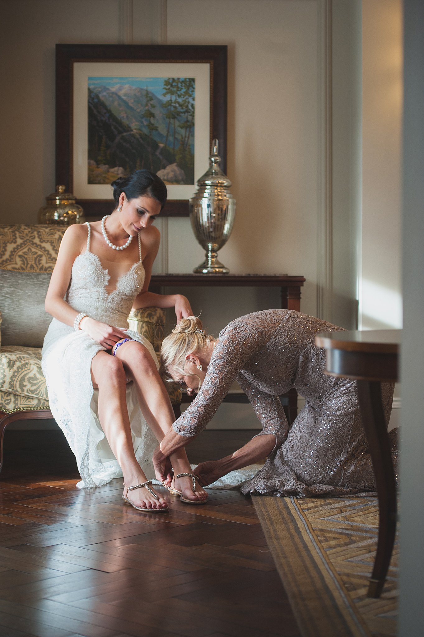 A woman helps the bride put on her shoes while sitting on a vintage couch at The Broadmoor Wedding