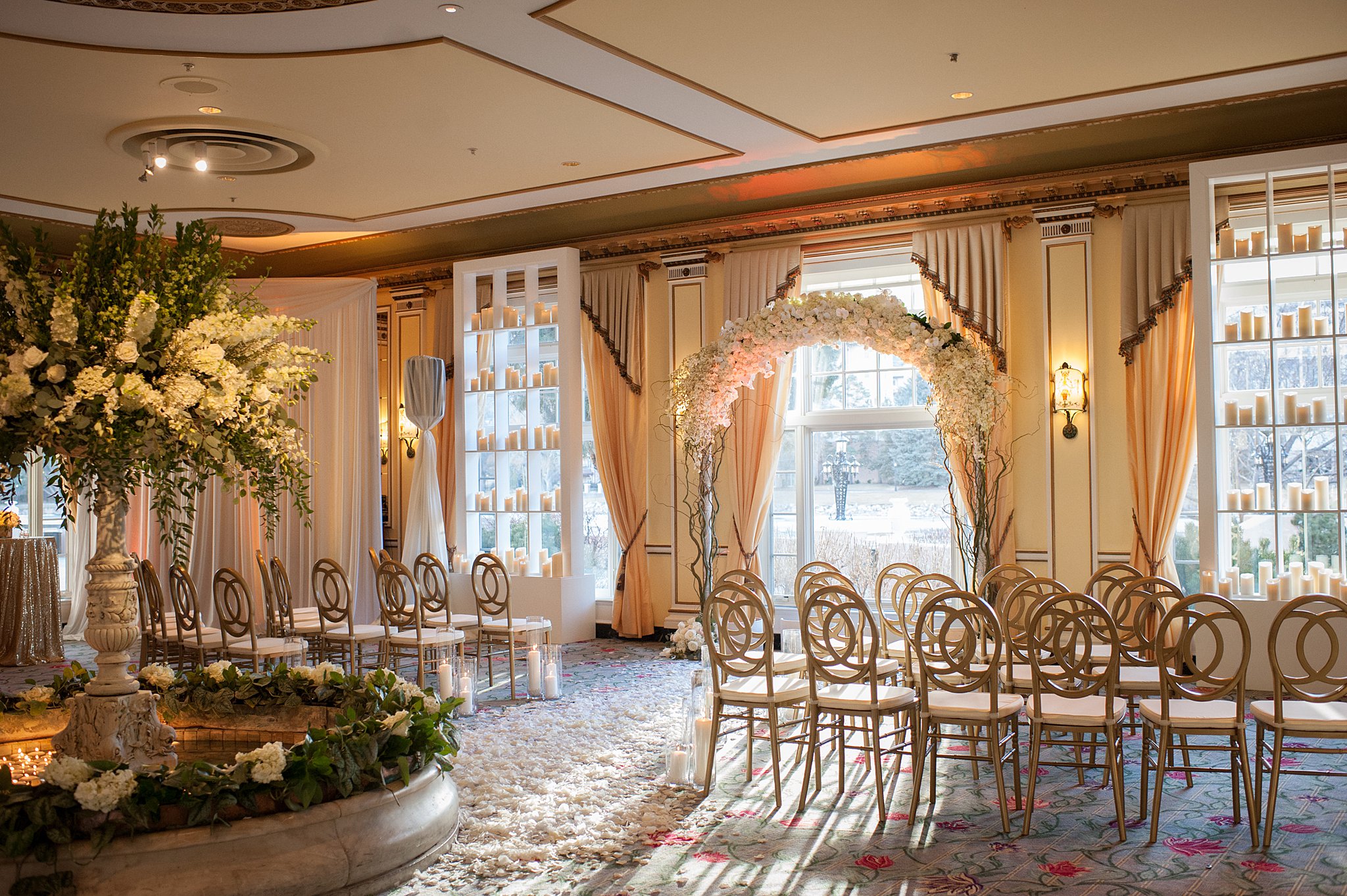 A view of an indoor wedding reception with gold chairs and floral arch at The Broadmoor Wedding venue