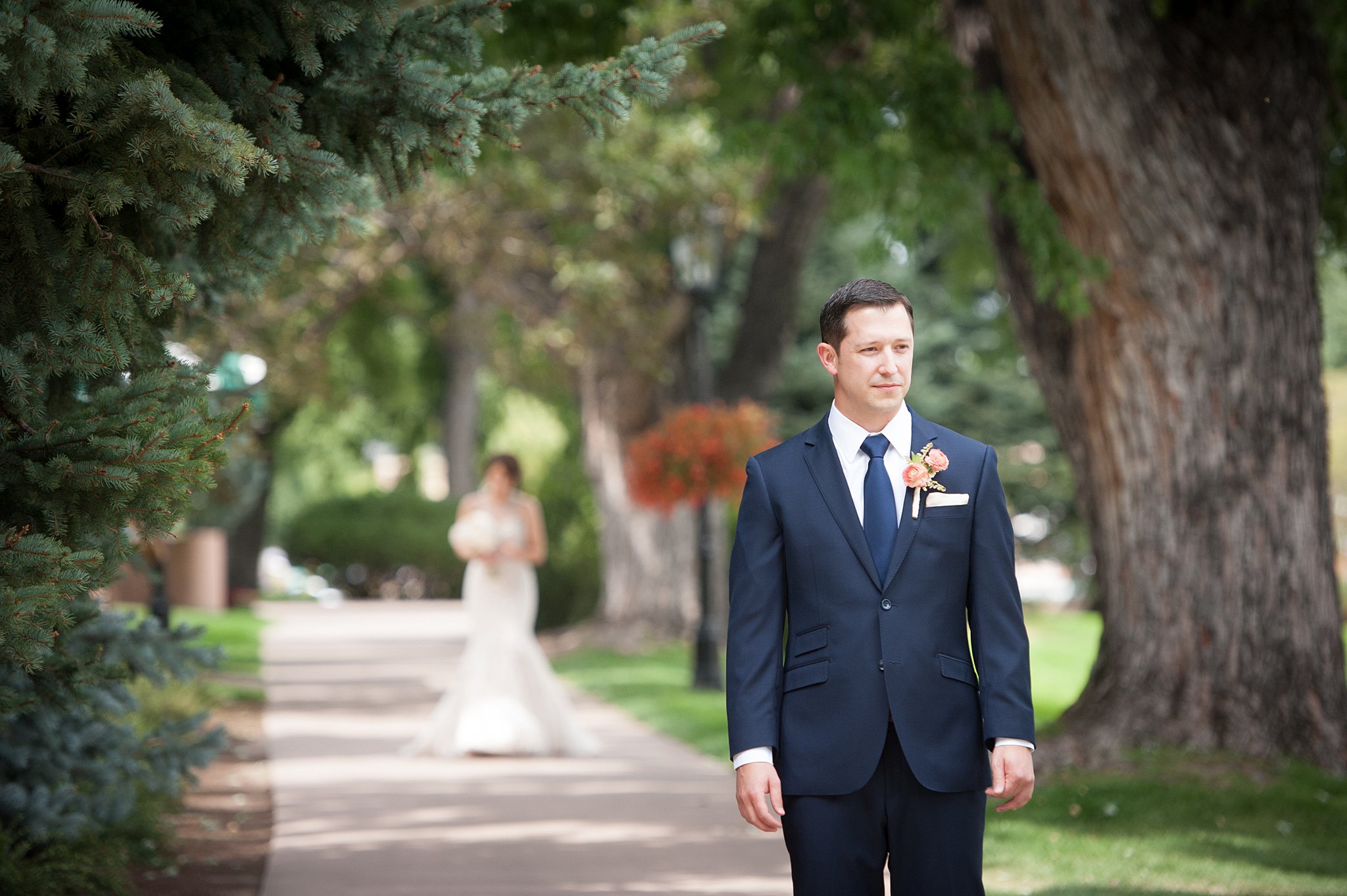 A groom nervously awaits his bride for their first look on a sidewalk under trees